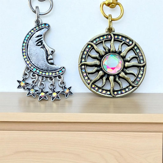 Sun and moon keychains with star accents on a wooden surface.