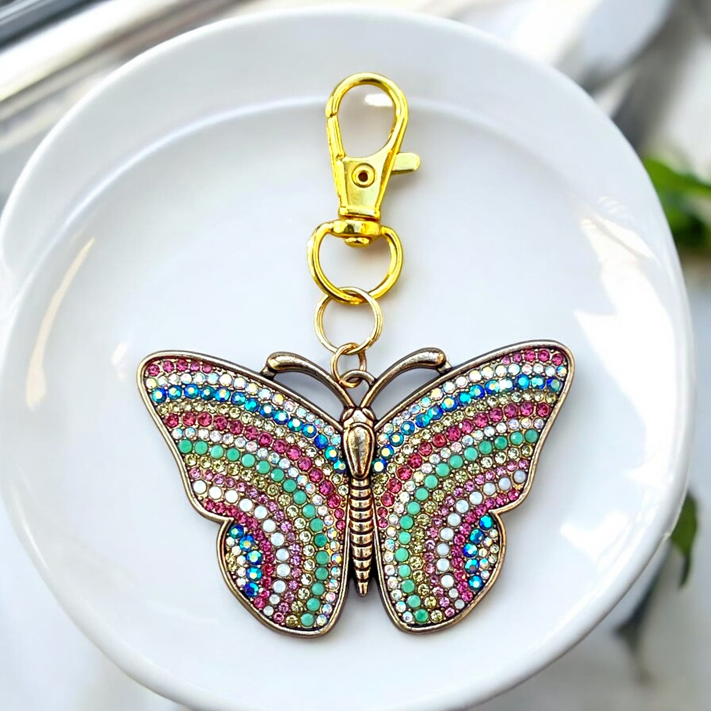 Butterfly charm with gold finish and multicolor wings on neutral background