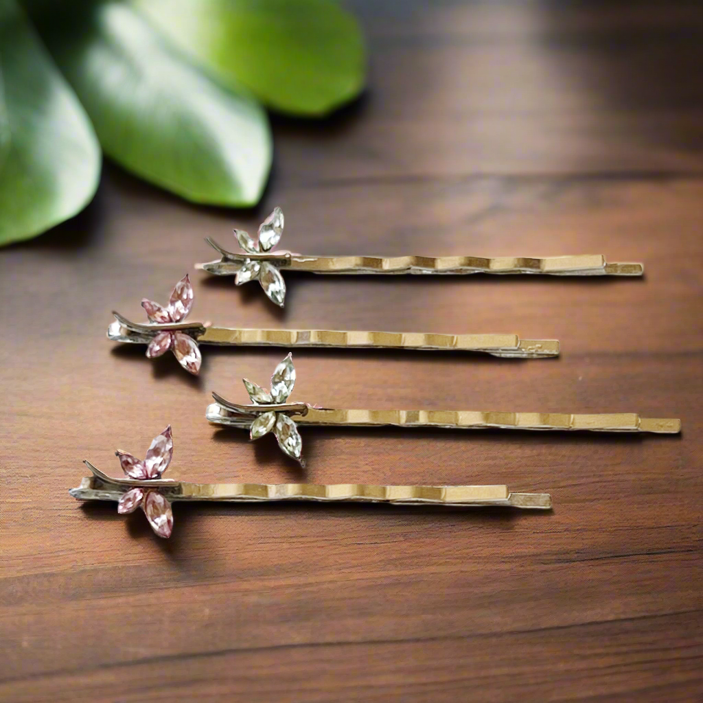 A set of four silver-colored dragonfly hair pins adorned with light green and pink rhinestones, displayed on a wooden surface.