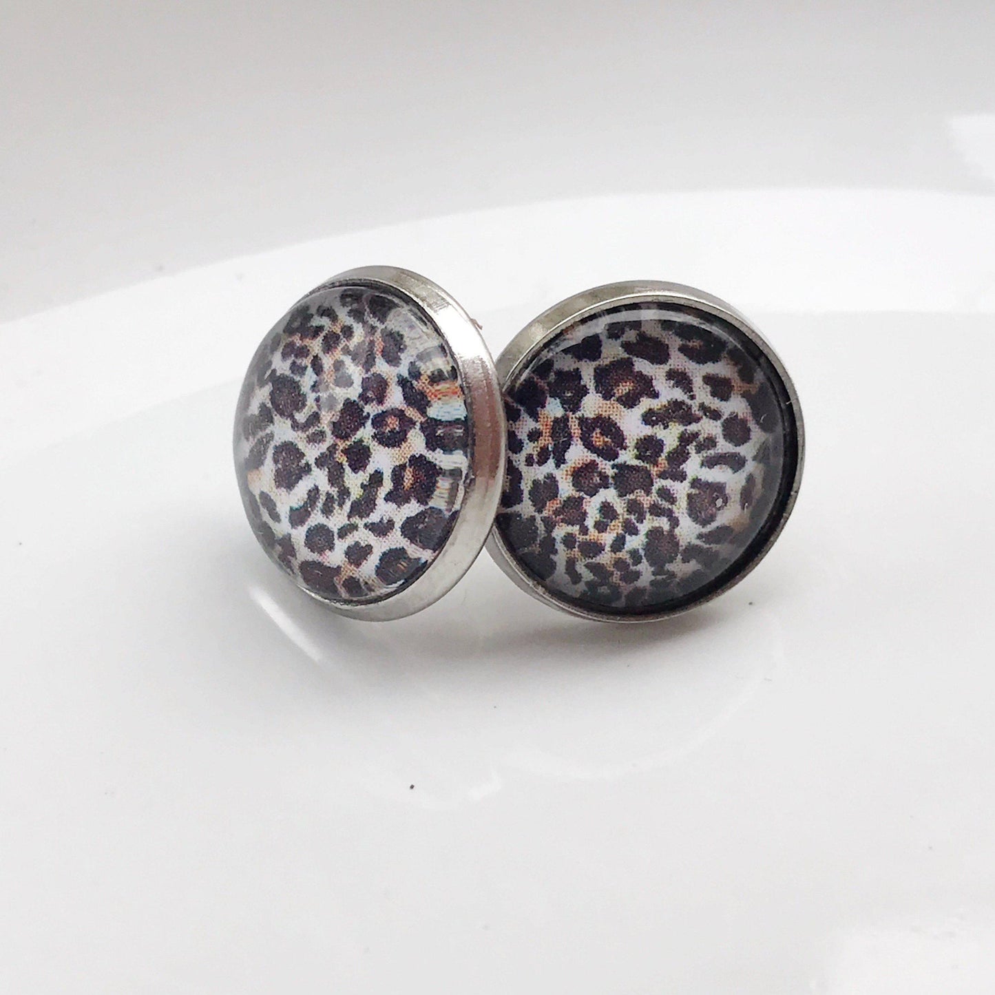 Handmade cheetah print stud earrings with silver bezel on white background