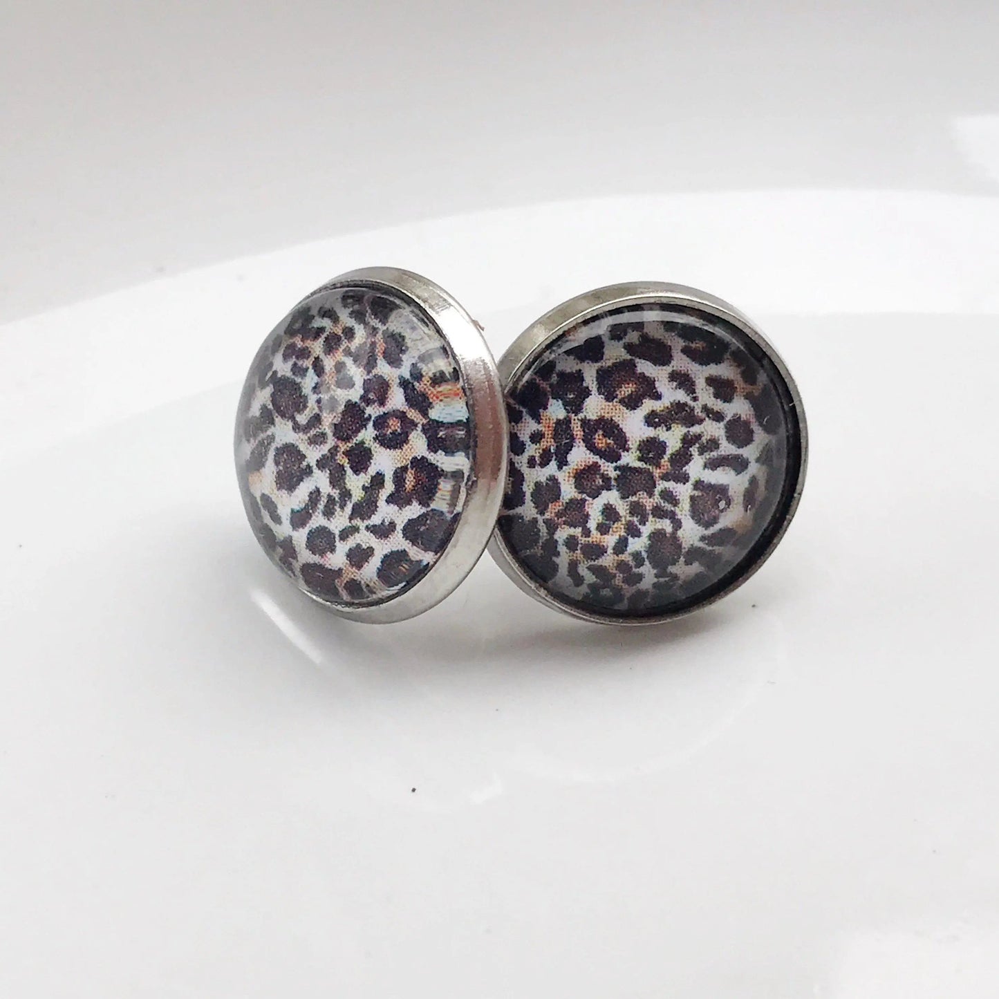 Handmade cheetah print stud earrings with silver bezel on white background
