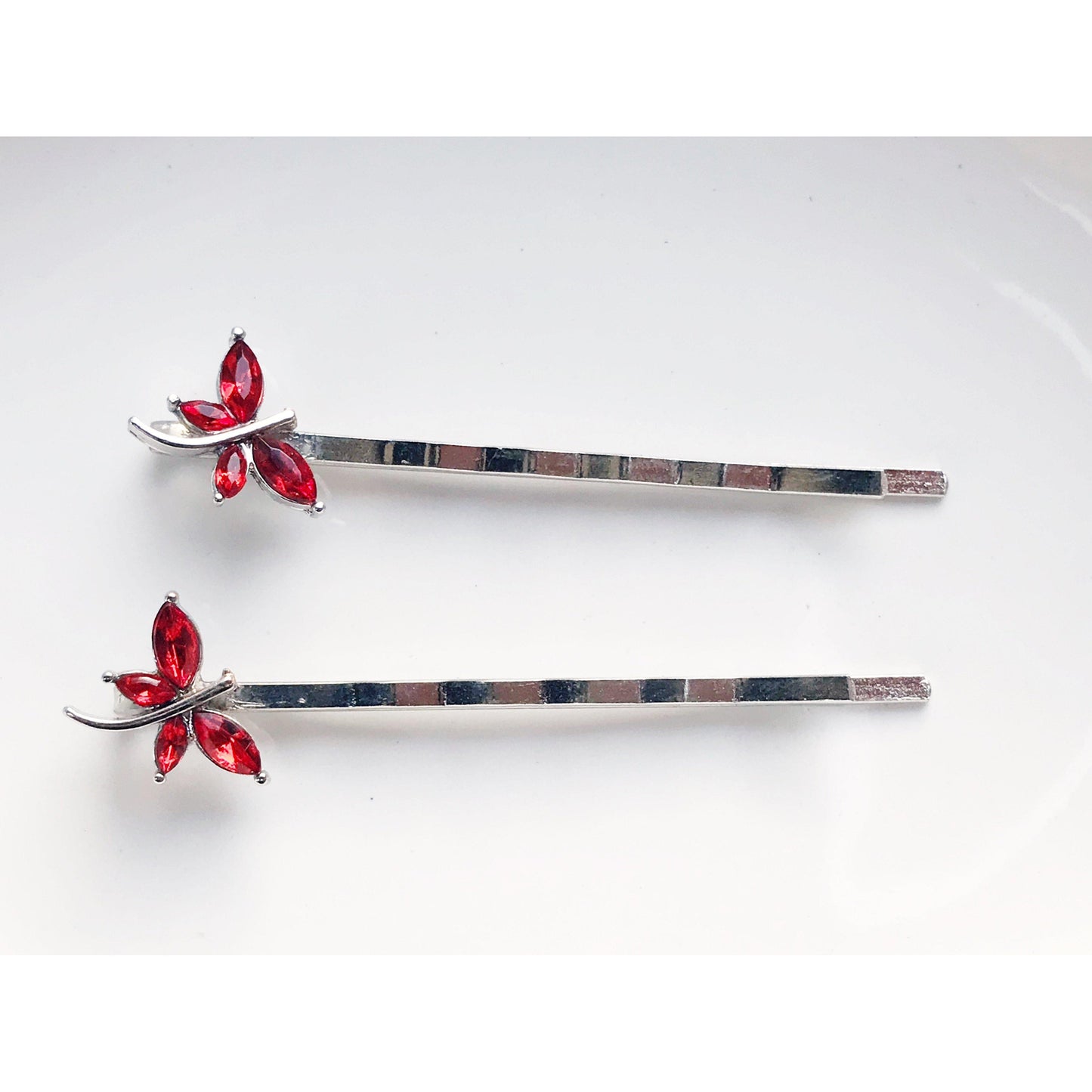 Whimsical red and silver dragonfly bobby pins displayed on stone slab