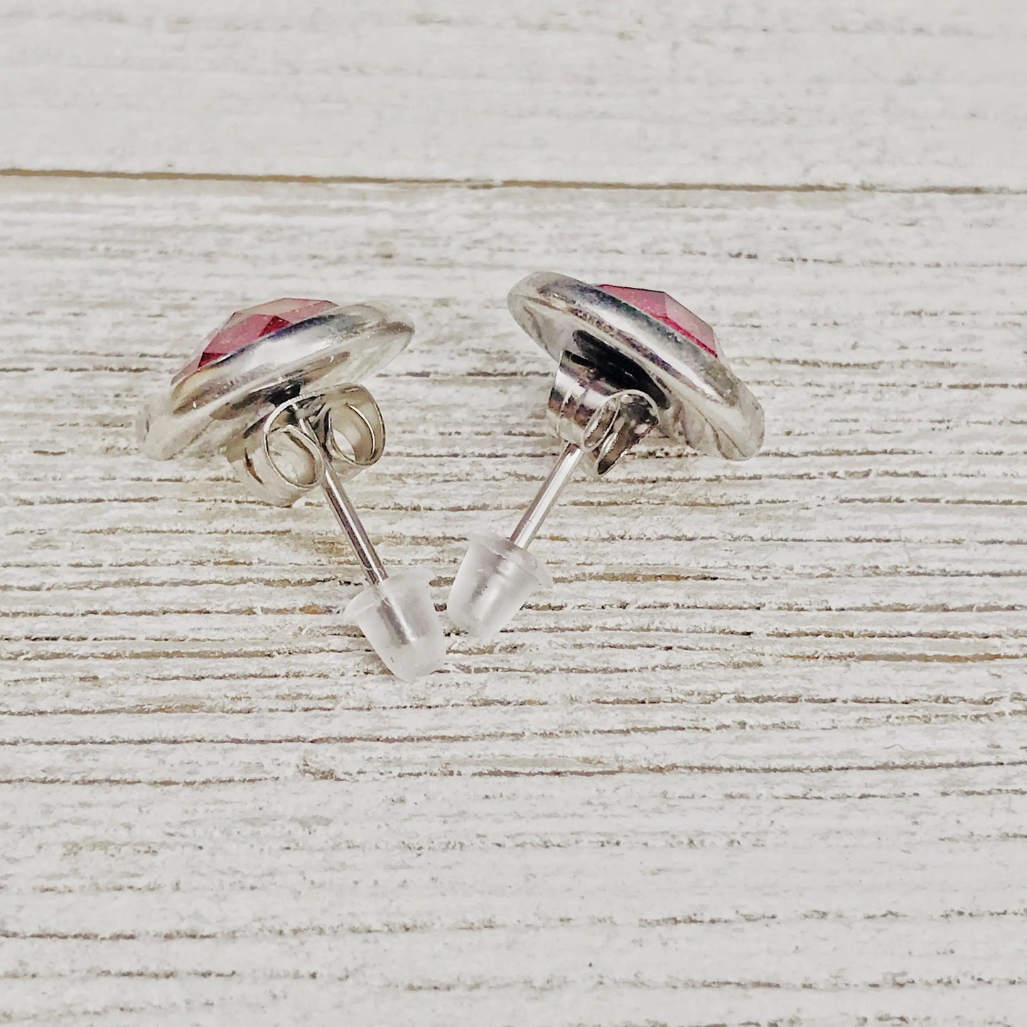 Back of round hot pink glitter stud earrings in a silver-tone setting displayed on a light wood surface