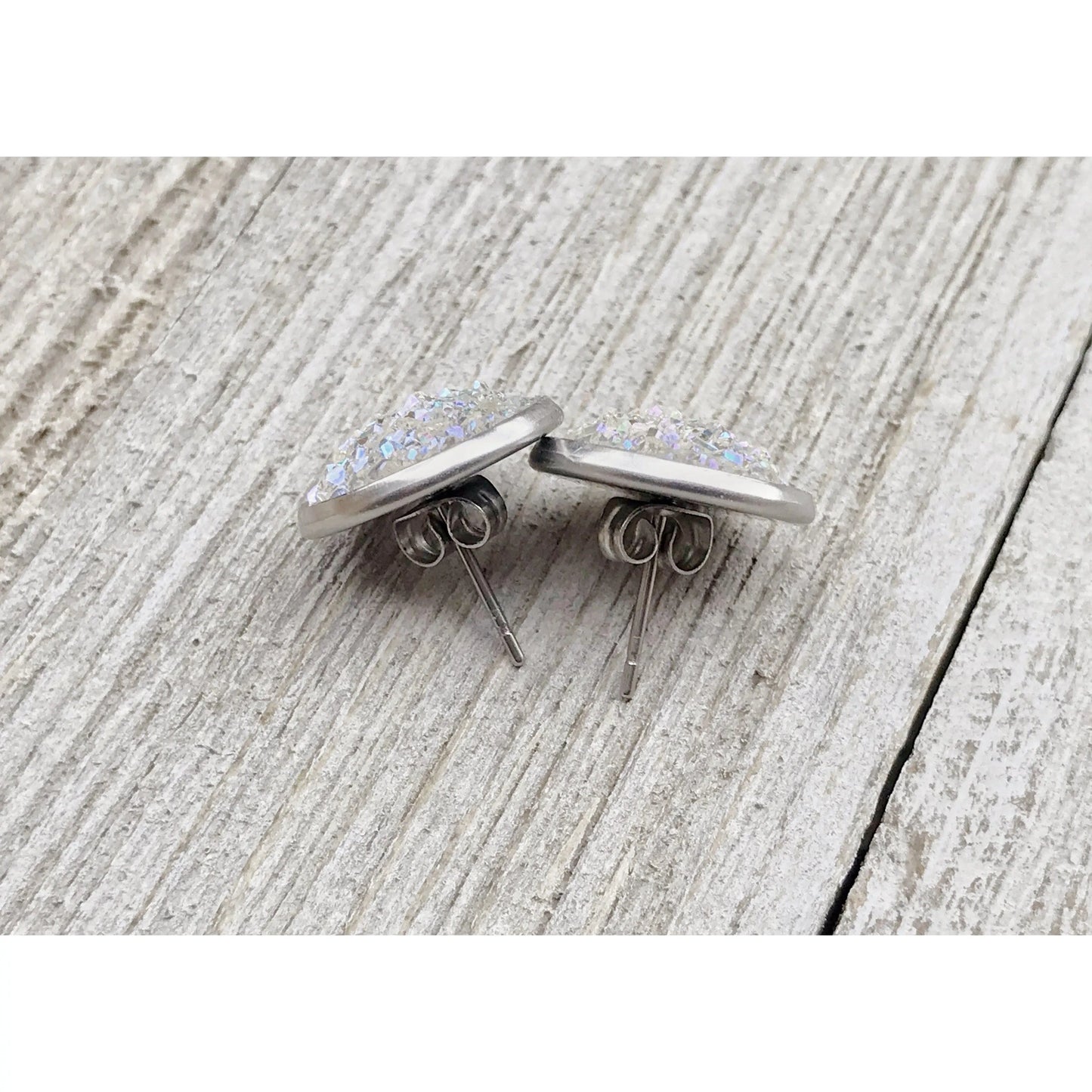 Back of a pair of silver earrings with glittery centers on a textured wooden surface