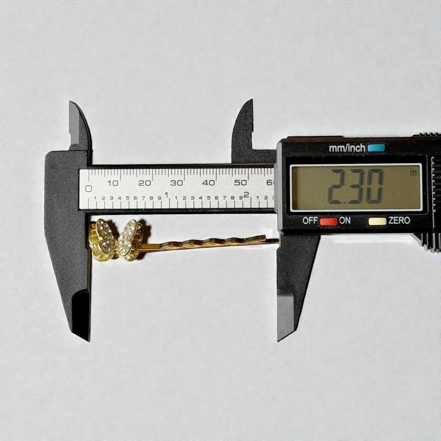 Digital caliper measuring a decorative hair pin with a white background