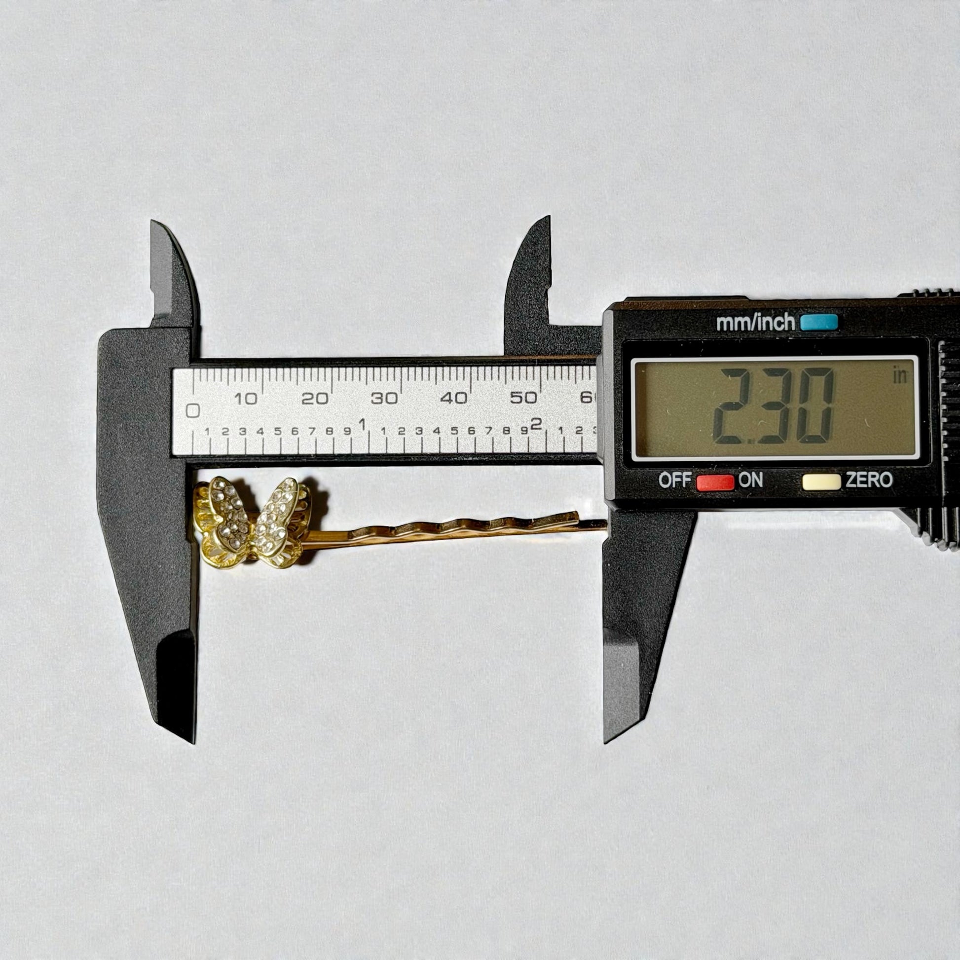 Digital caliper measuring a decorative hair pin with a white background