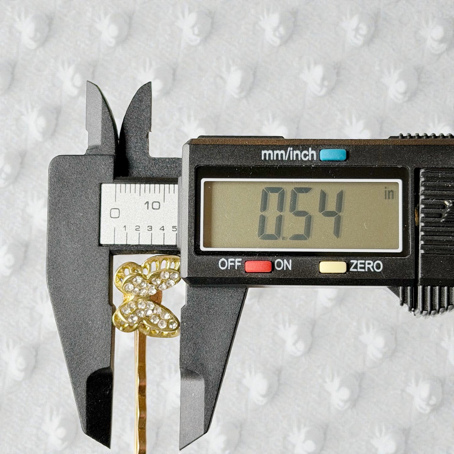 Digital caliper measuring a gold flower-shaped object against a textured gray background