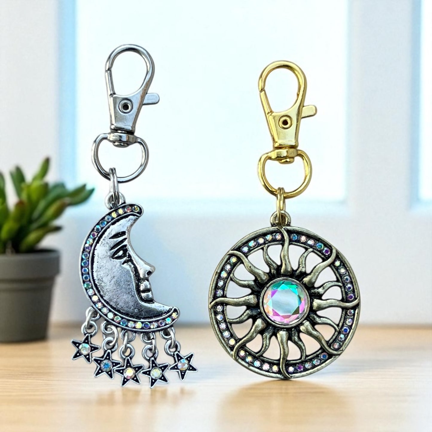 Two decorative keychains with a moon and star design and a sun and gemstone design on a blurred background.