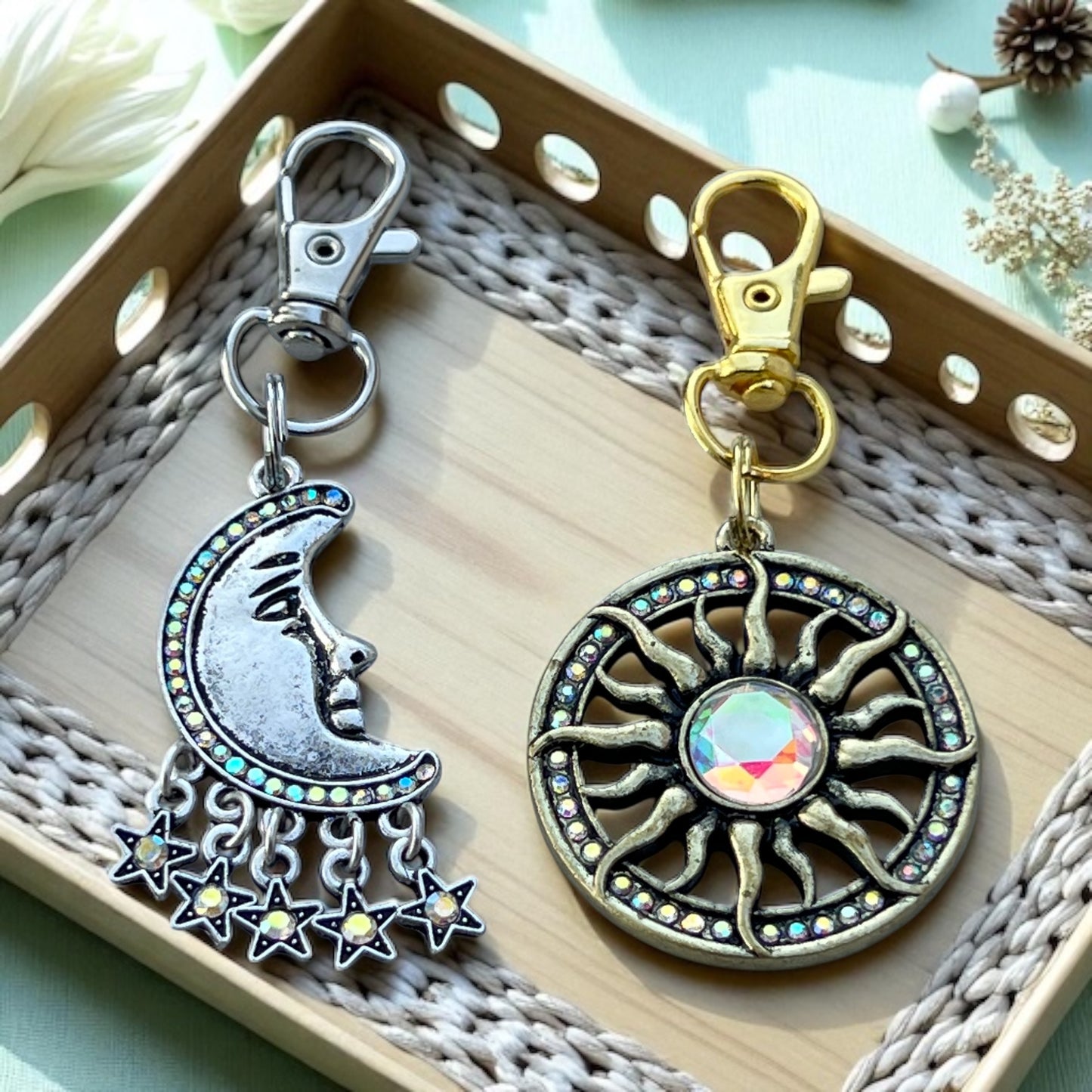 Two decorative keychains, one with a moon and stars design and the other with a sun and star design, on a textured surface.