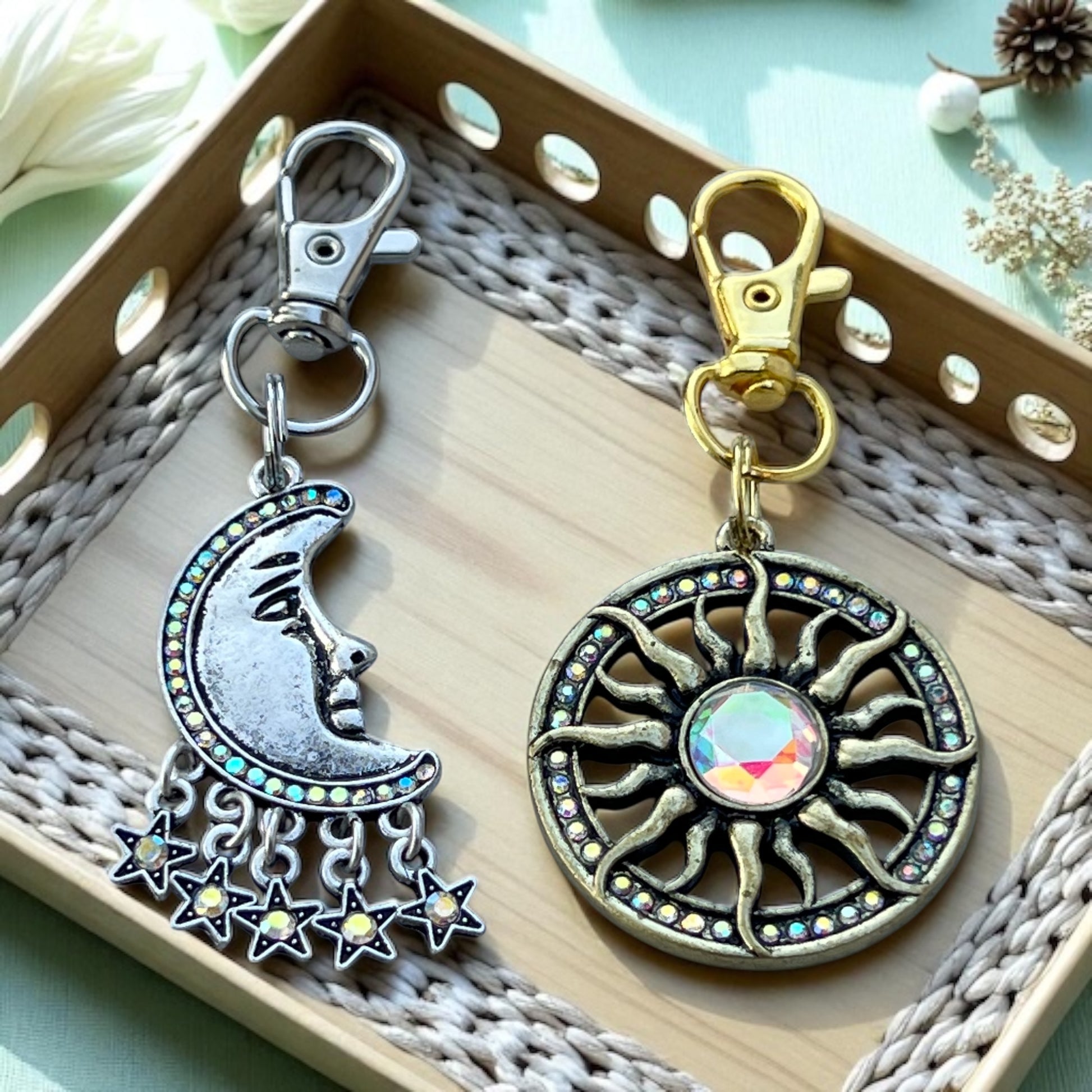 Two decorative keychains, one with a moon and stars design and the other with a sun and star design, on a textured surface.