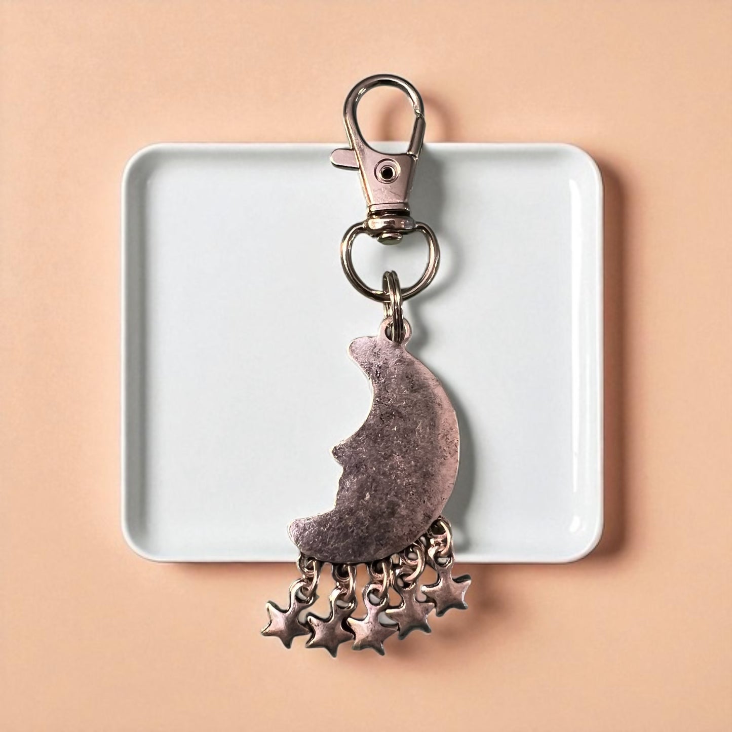 Backside of Keychain with moon and star charms on a white tray against a beige background