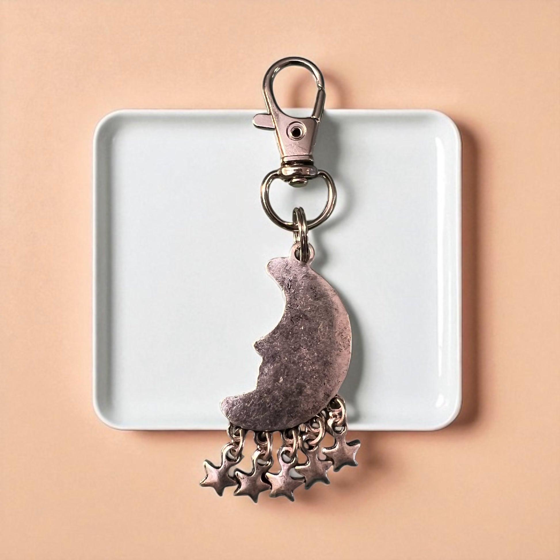 Backside of Keychain with moon and star charms on a white tray against a beige background