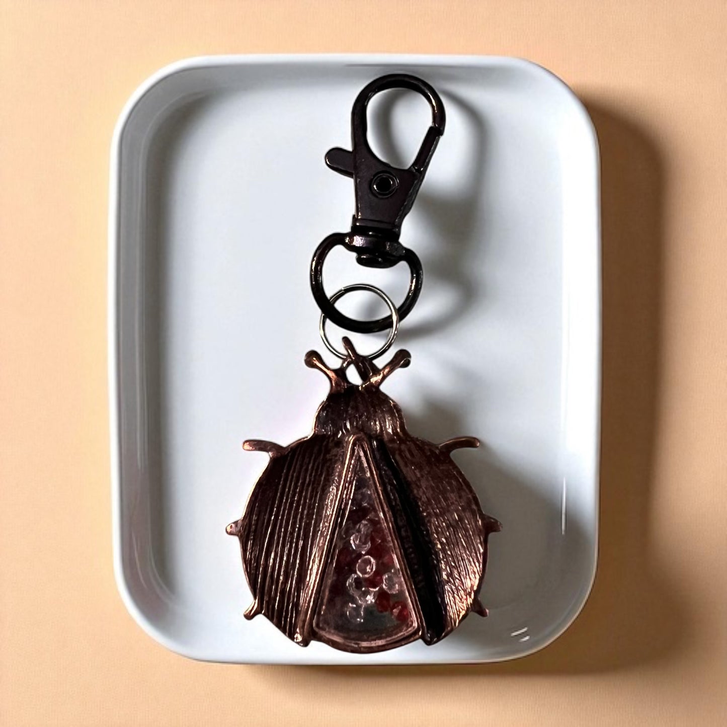 Backside of ladybug keychain on a white tray with a beige background