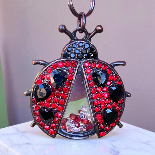 Keychain shaped like a ladybug with red and black gemstones on a white surface.