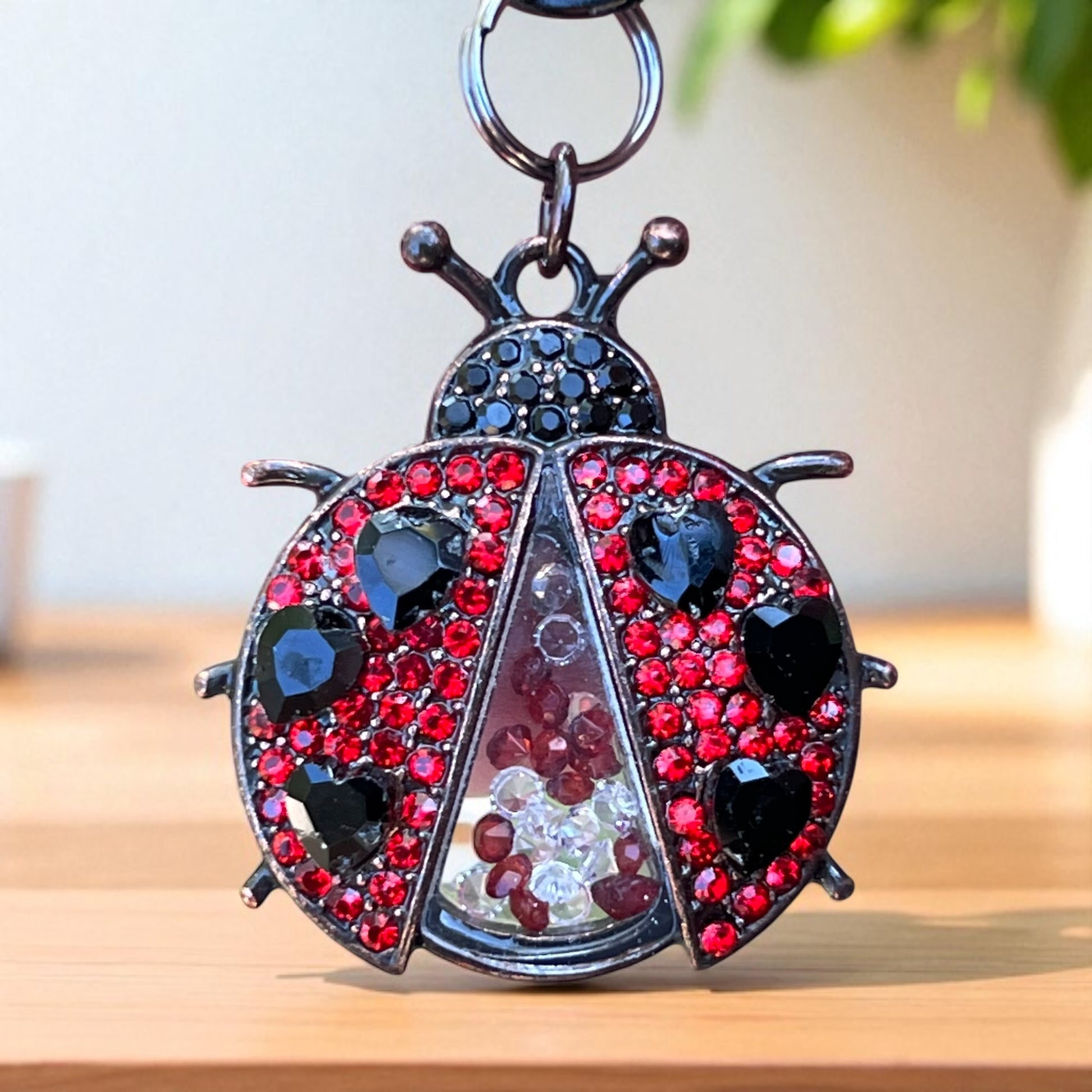 Decorative ladybug keychain with red and black gemstones on a wooden surface.