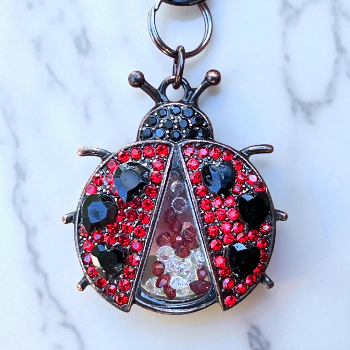 Keychain shaped like a ladybug with red and black gemstones on a marble background