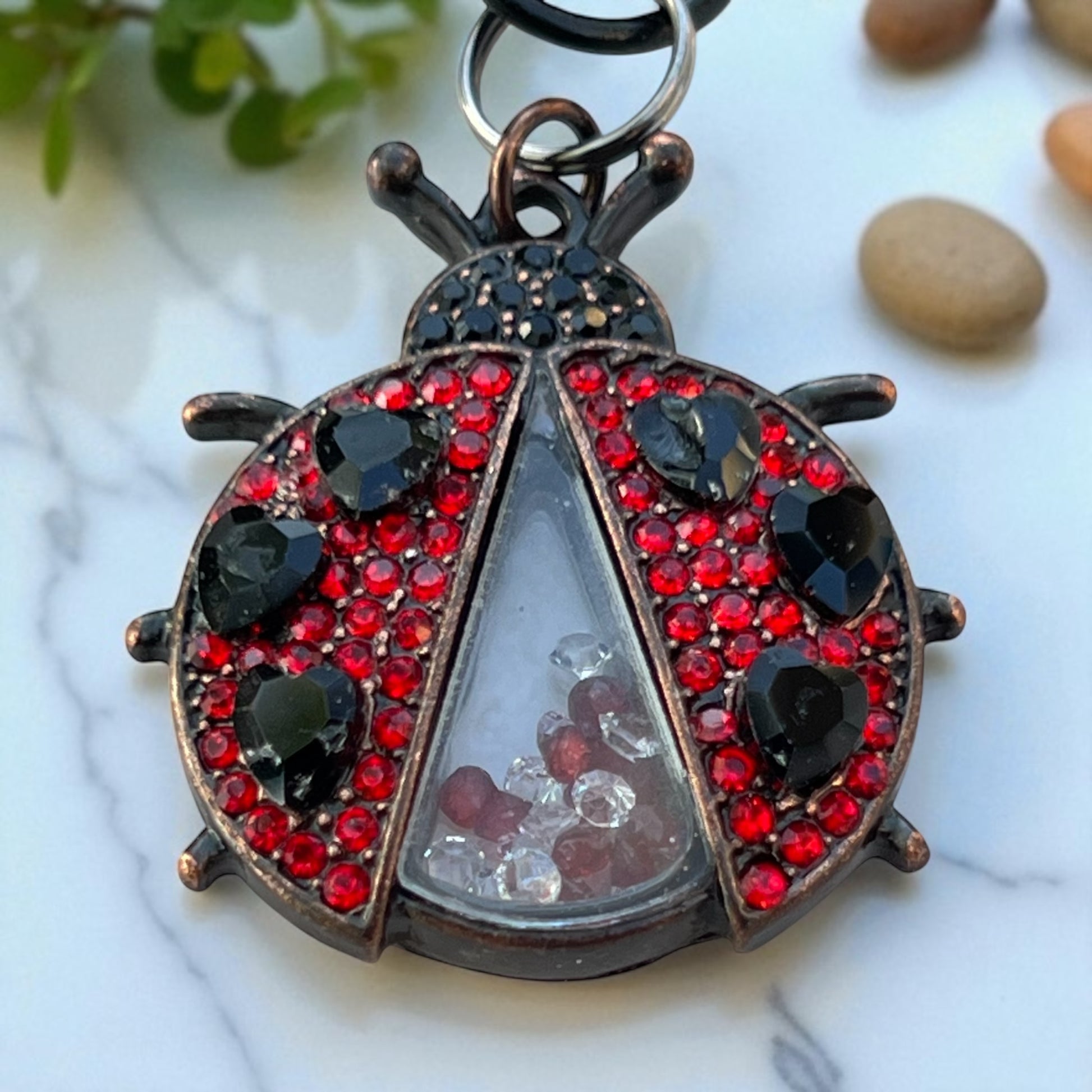 Decorative ladybug keychain with red and black gemstones on a marble surface.