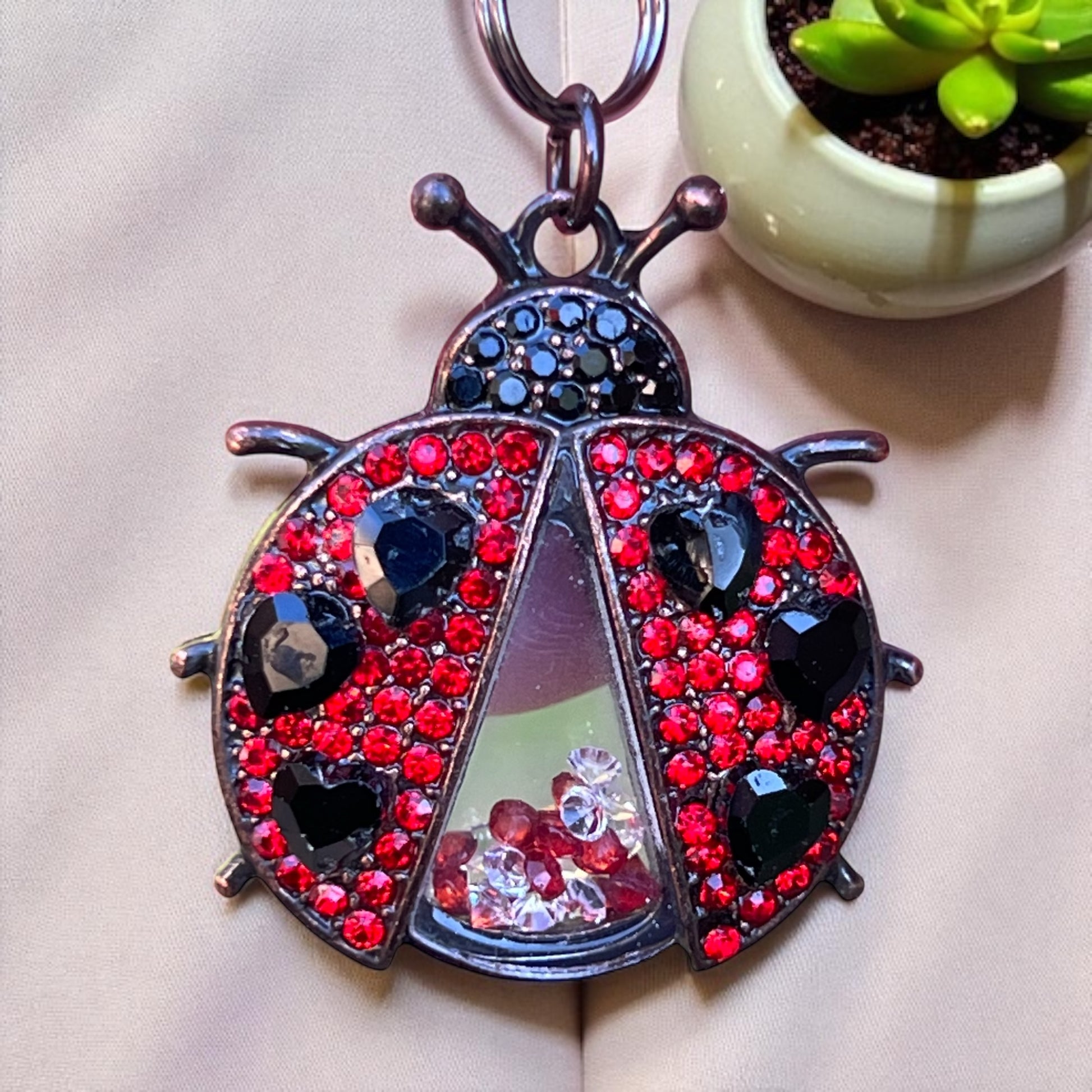Decorative keychain shaped like a ladybug with red and black gemstones on a beige surface.