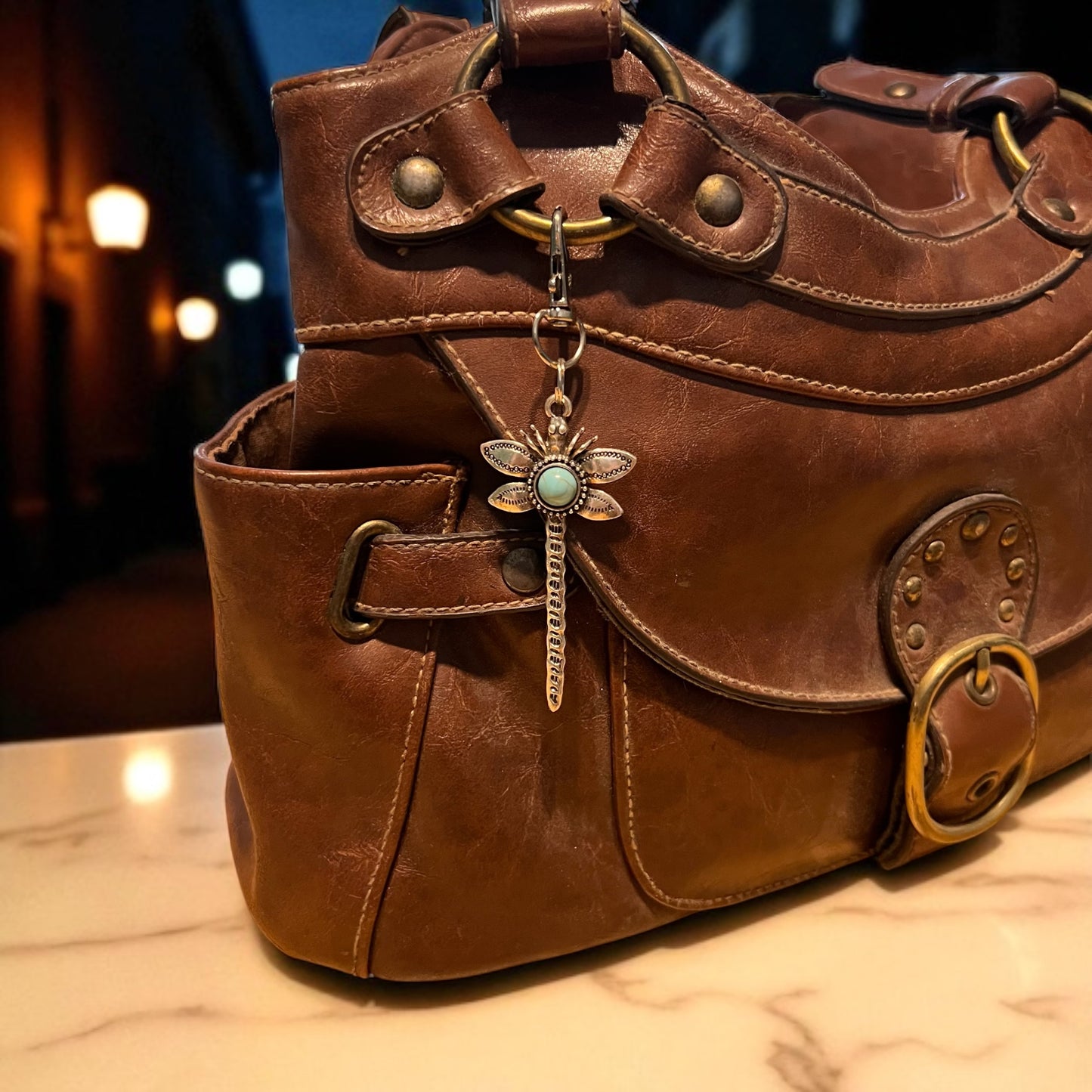 Brown leather handbag with a decorative dragonfly charm on a blurred background