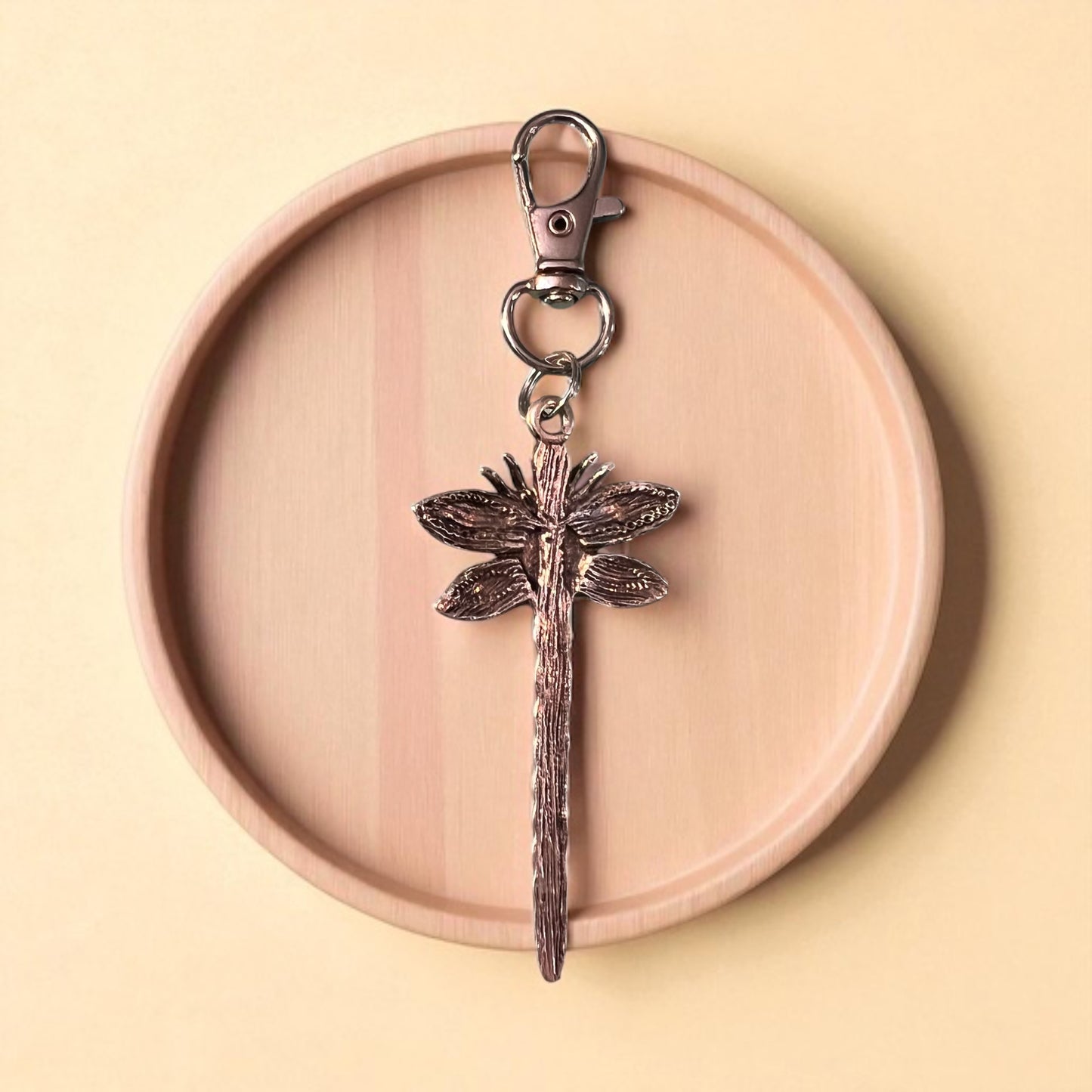 backside of silver dragonfly keychain on a wooden plate with a beige background