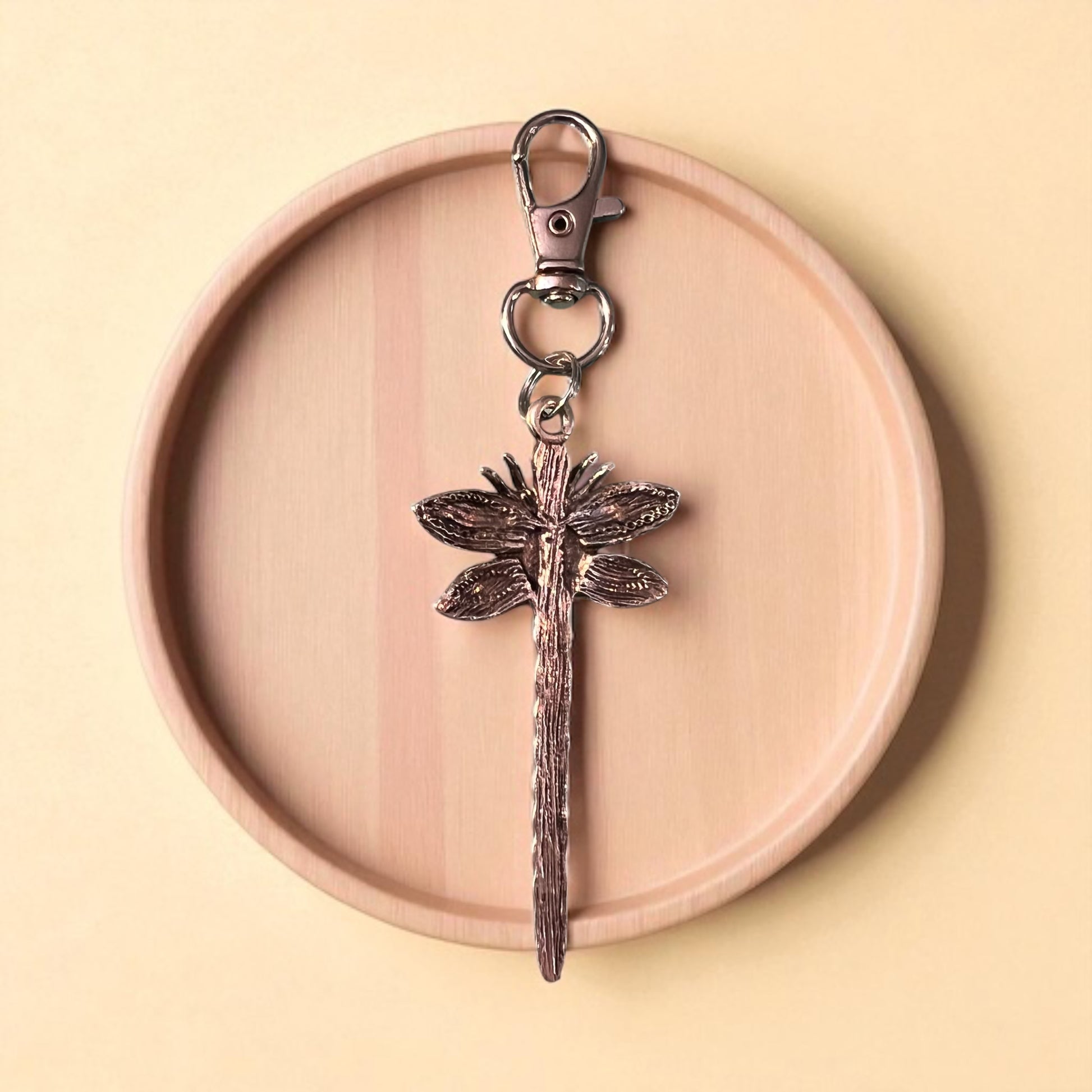 backside of silver dragonfly keychain on a wooden plate with a beige background