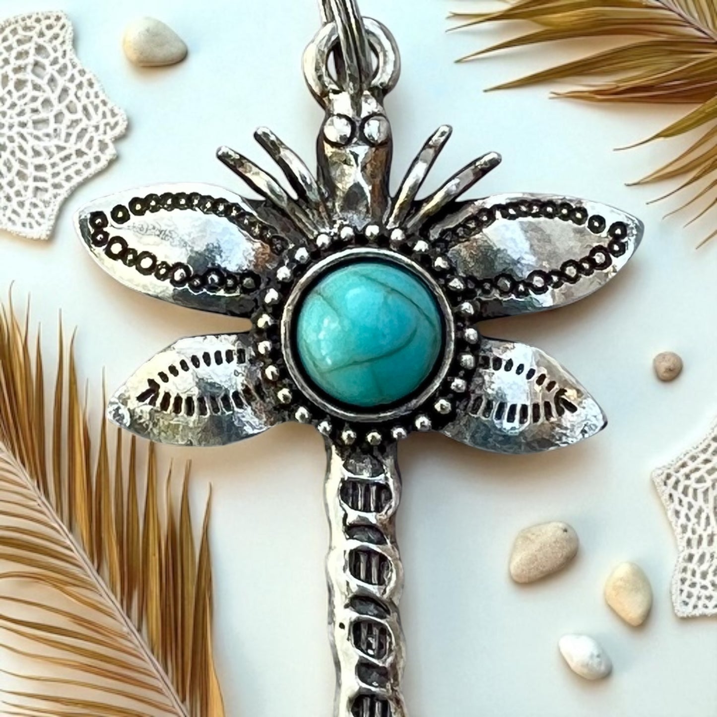 Silver Dragonfly purse charm with turquoise stone on a light background with feathers and stones