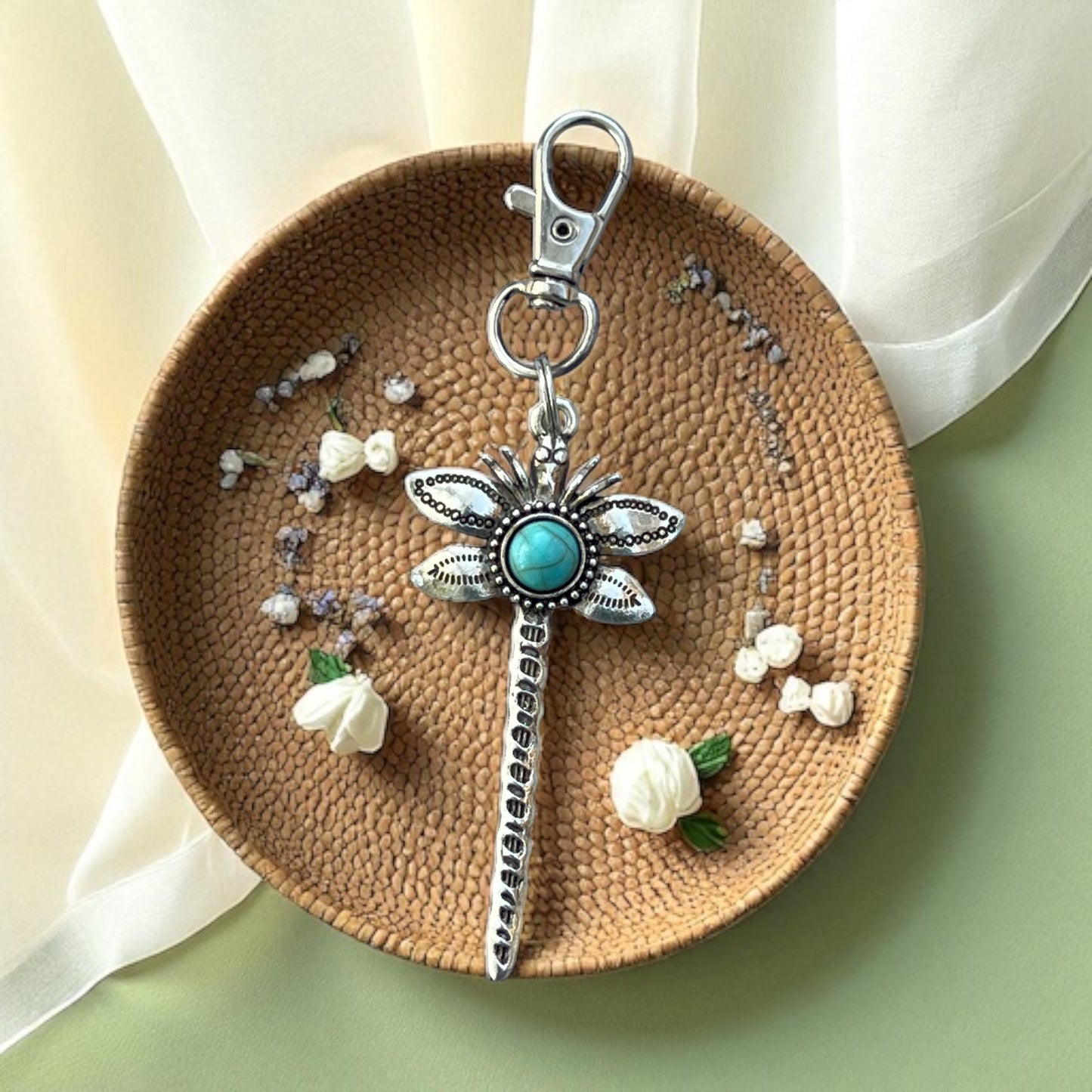 Decorative dragonfly keychain with turquoise stone on a woven plate with flowers