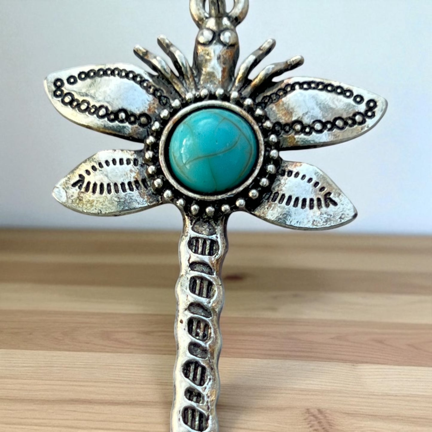 Silver dragonfly keychain charm with turquoise stone on a wooden surface