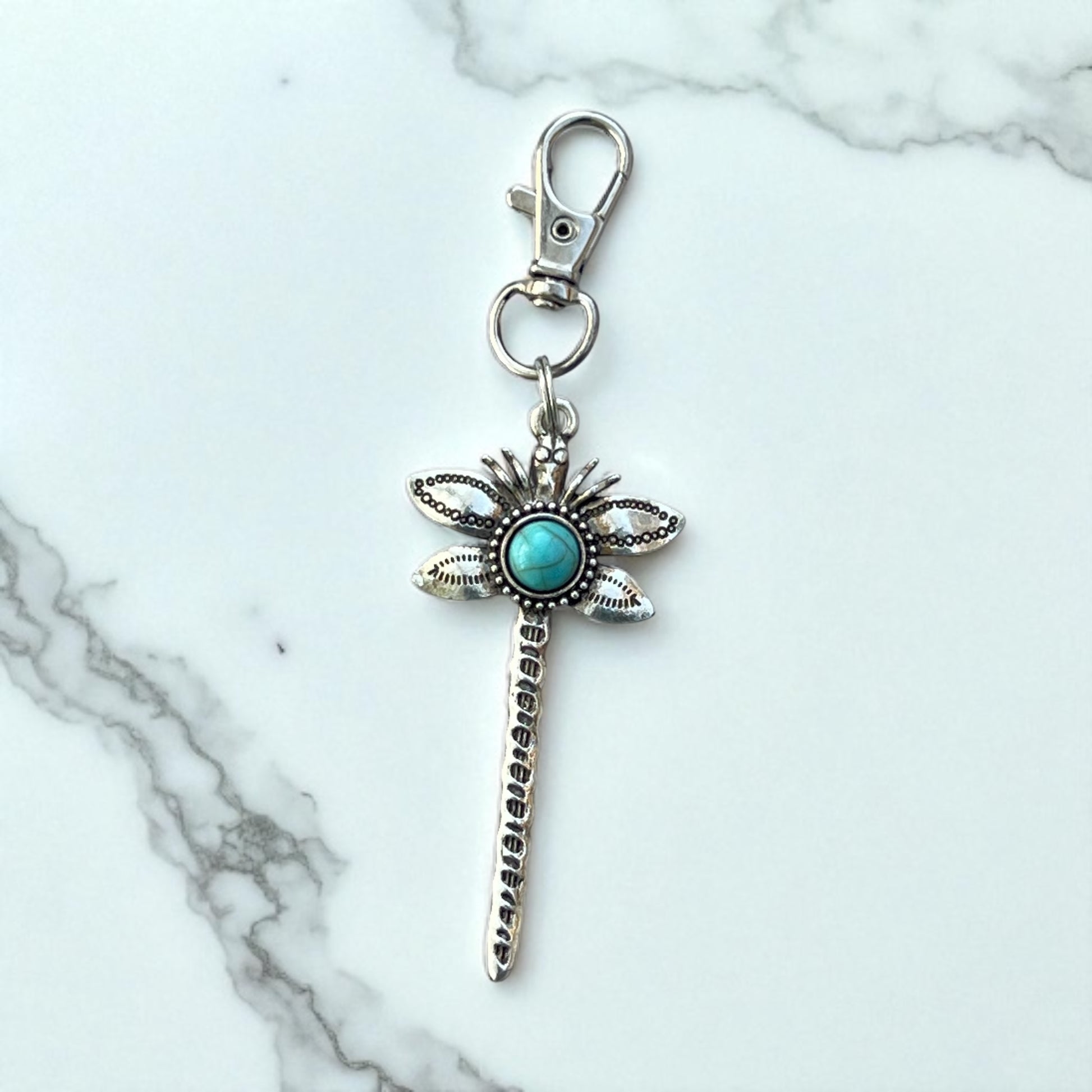 Silver dragonfly keychain with turquoise stone on a marble background