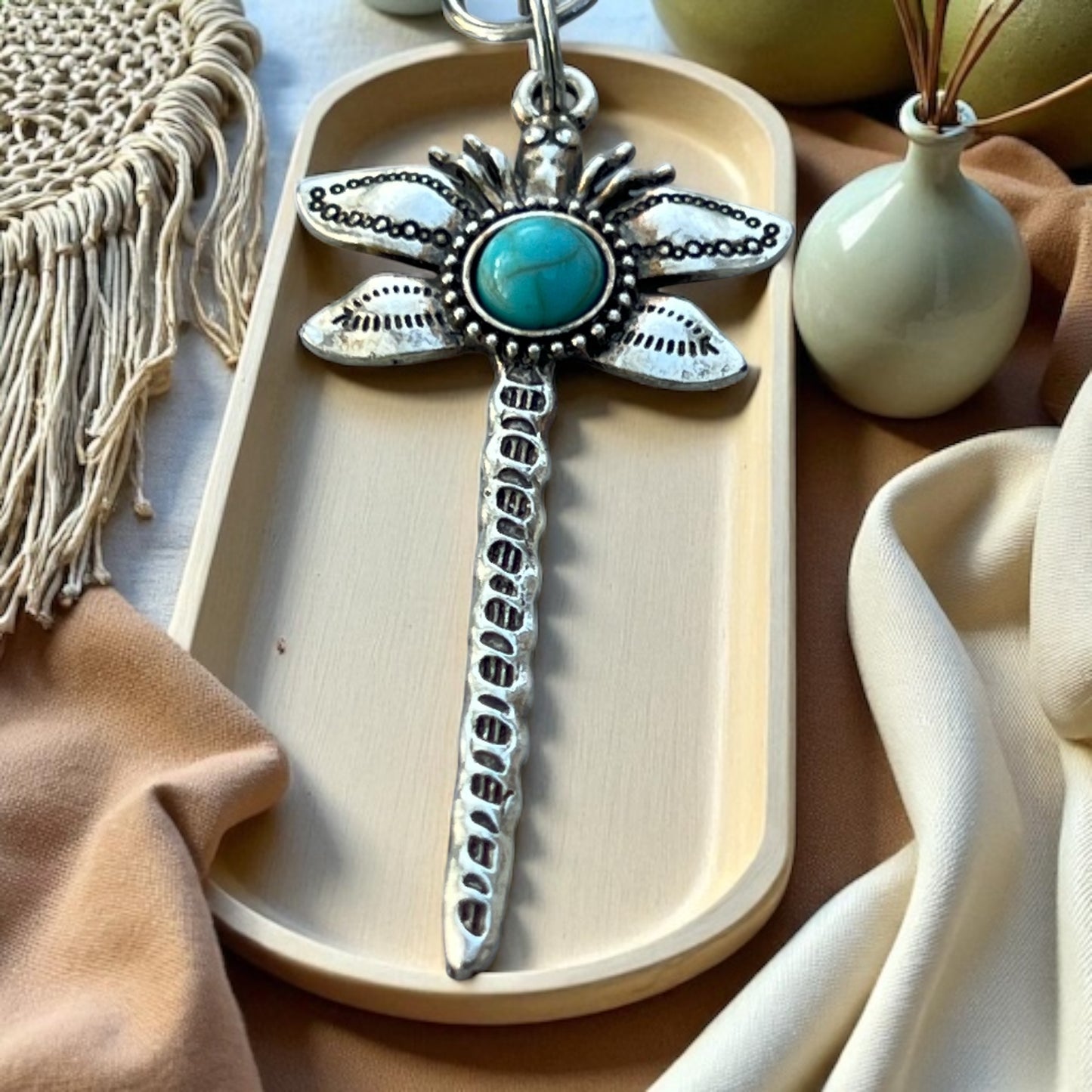 Decorative dragonfly keychain with turquoise stone on a wooden tray with a neutral background