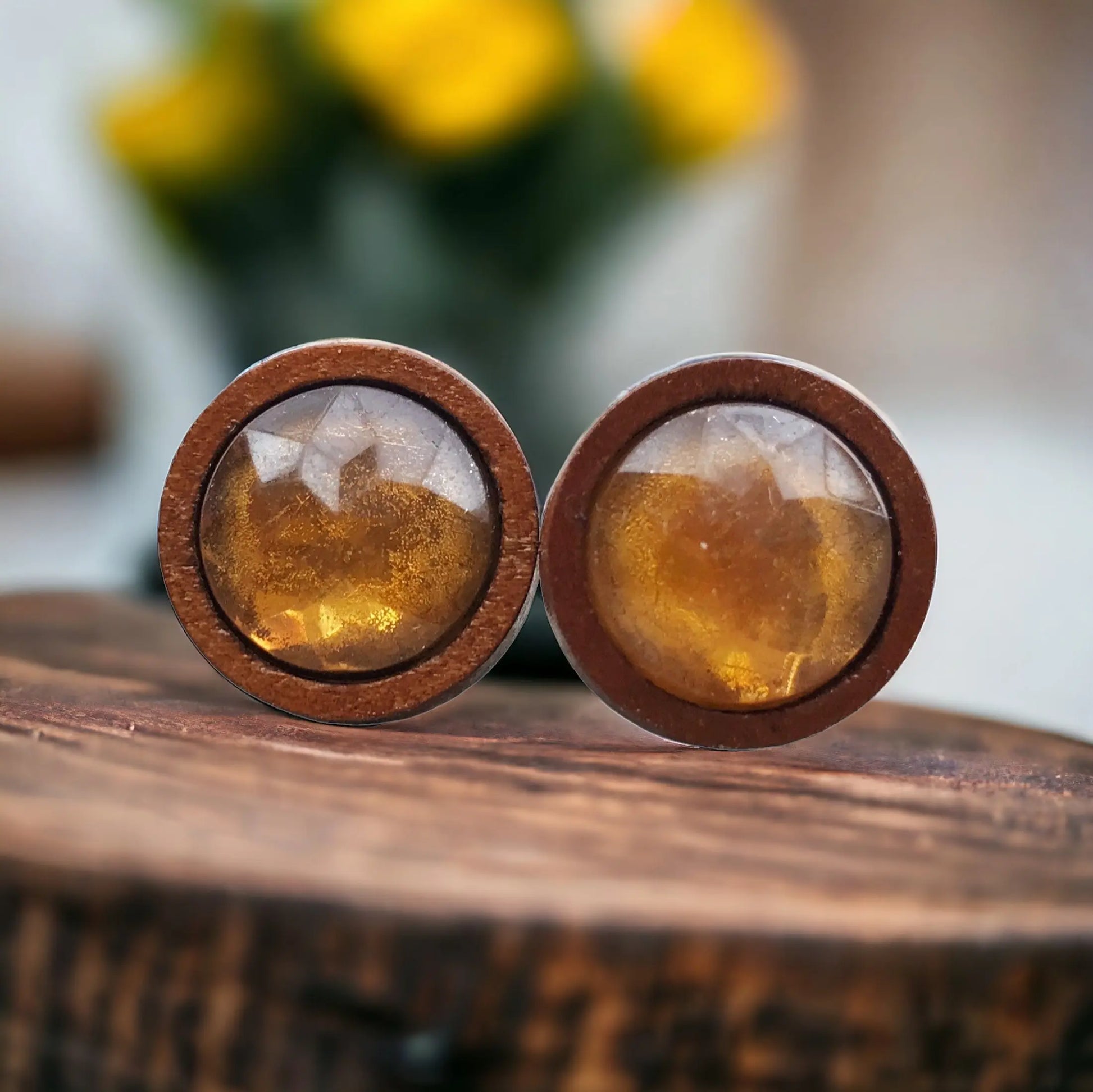 Round wooden earrings with amber-colored stones on a wooden surface.