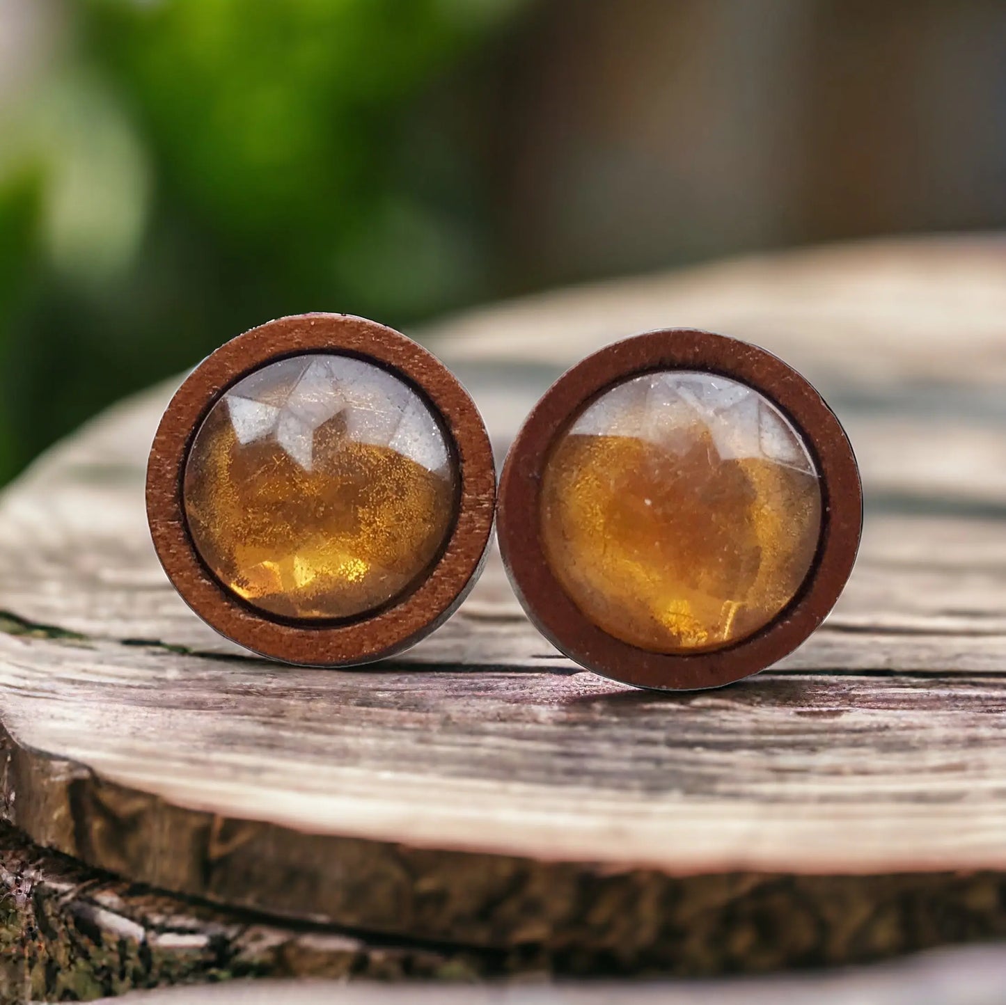 Round amber honey brown faceted stud earrings in a wood setting displayed on a rustic wood slice