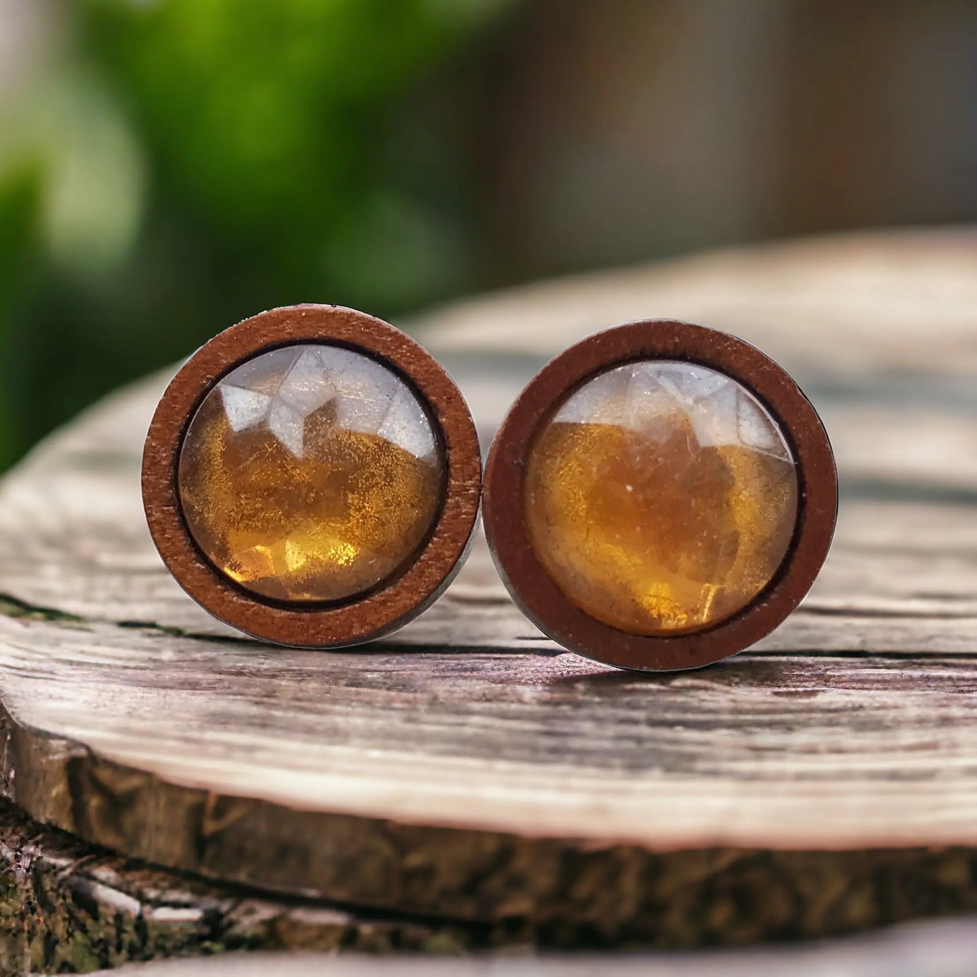 Round amber honey brown faceted stud earrings in a wood setting displayed on a rustic wood slice