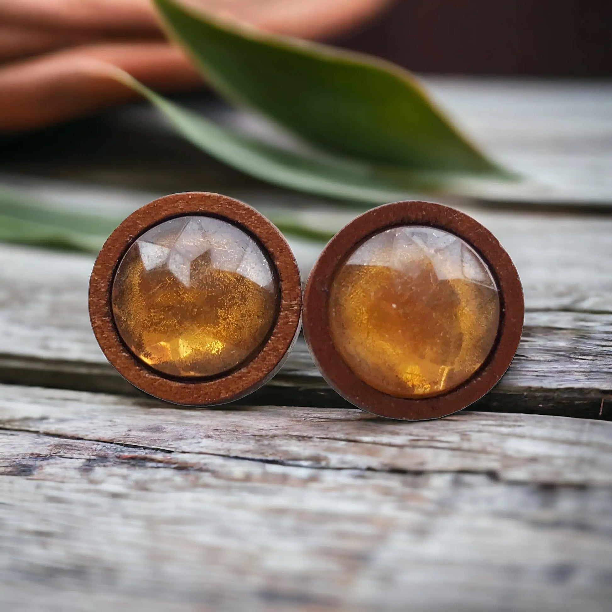Round wooden earrings with amber-colored stones on a wooden surface.