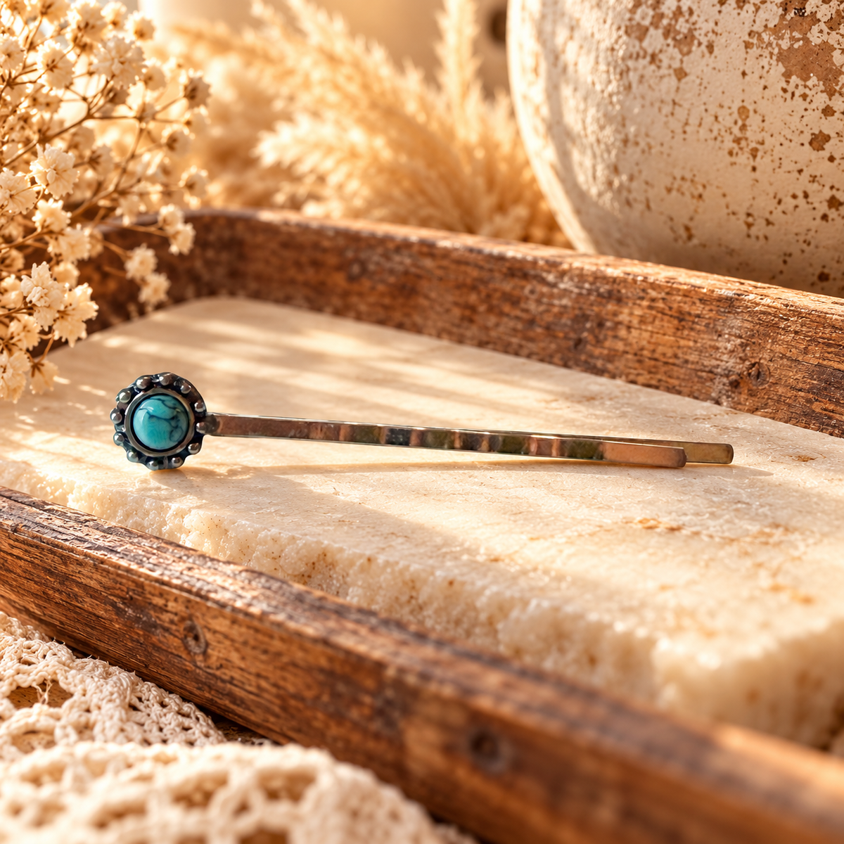 One silver-tone faux-turquoise western hair pin styled on a warm cream stone tray with rustic wood and dried ivory flowers; styled illustration
