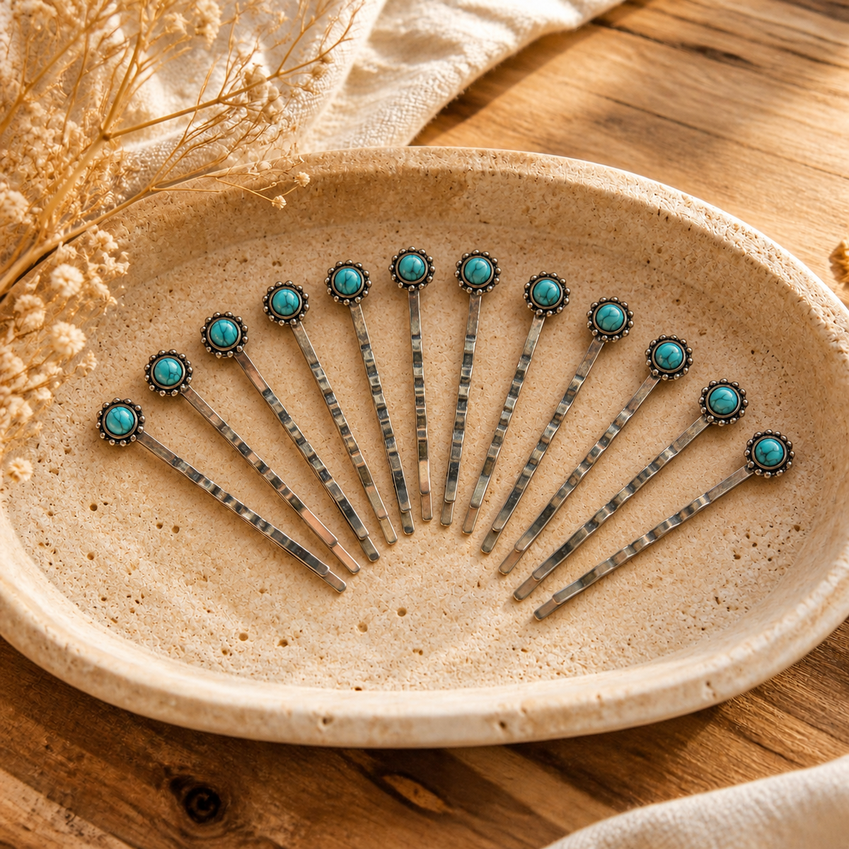 Exactly twelve silver-tone bobby pins with small round faux-turquoise stones resting inside a warm ivory travertine tray; styled lifestyle illustration
