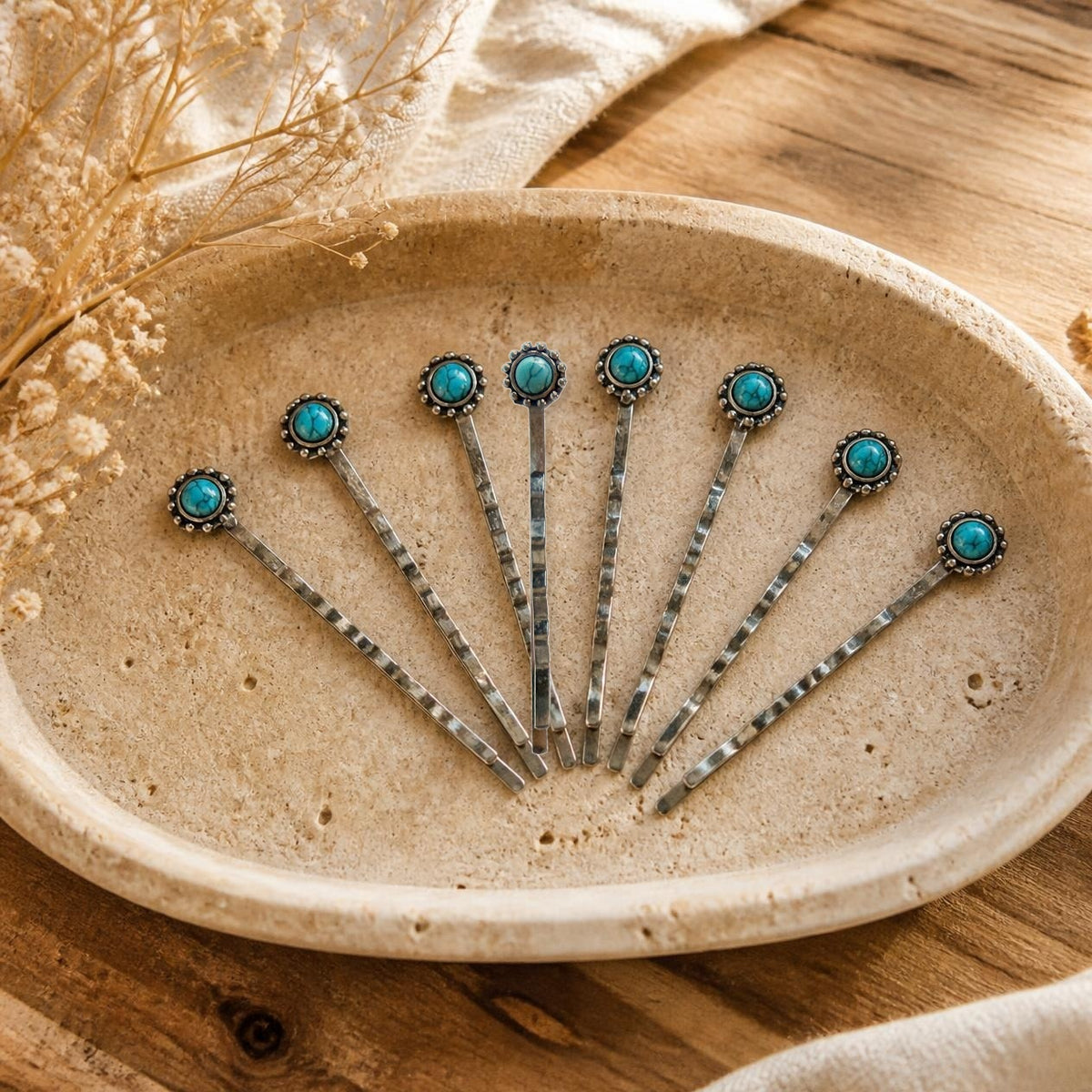 Exactly eight silver-tone western bobby pins with small round faux-turquoise stones styled on a warm cream stone tray; illustrative product composite