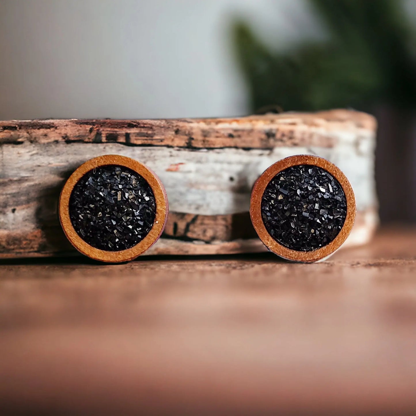 Front view of round black druzy wood stud earrings displayed on a rustic wood surface