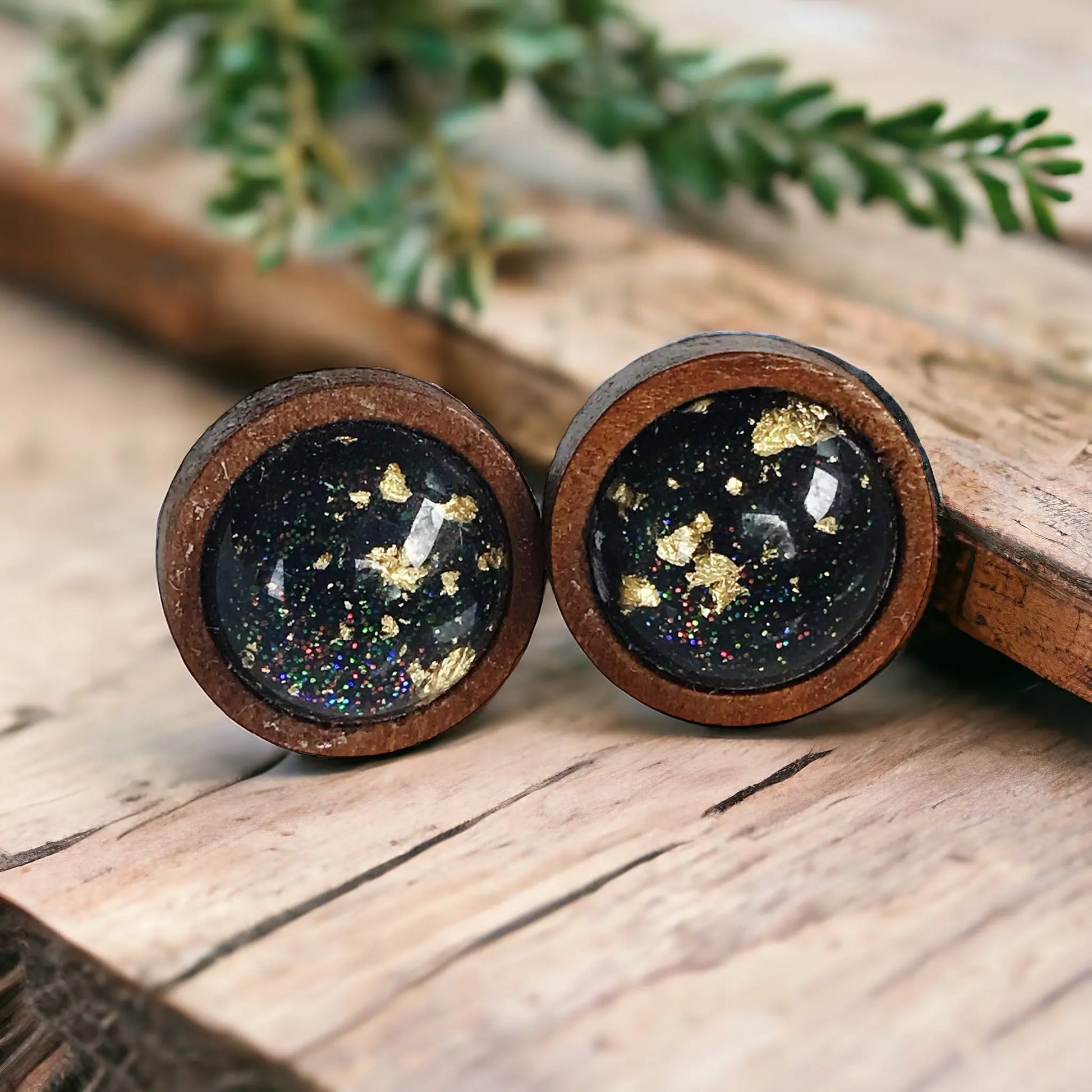 Round black resin wood stud earrings with gold flake detail and subtle sparkle on a boho wood background