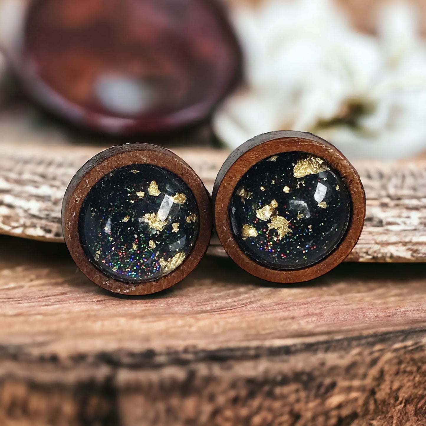 Close-up of round black resin wood stud earrings with gold flake detail and subtle sparkle on a boho wood background