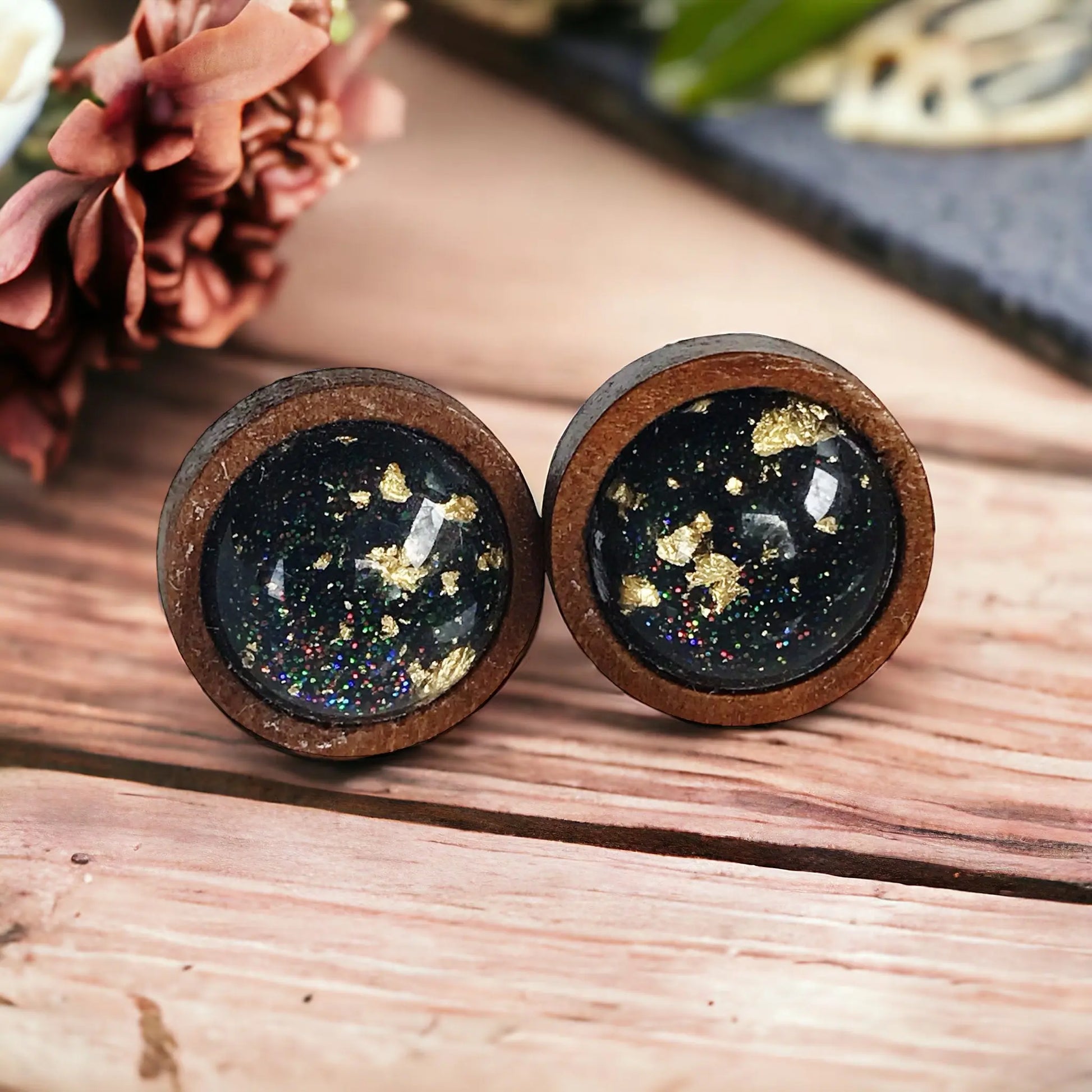 Round black resin wood stud earrings with gold flake detail and subtle sparkle on a rustic boho wood background