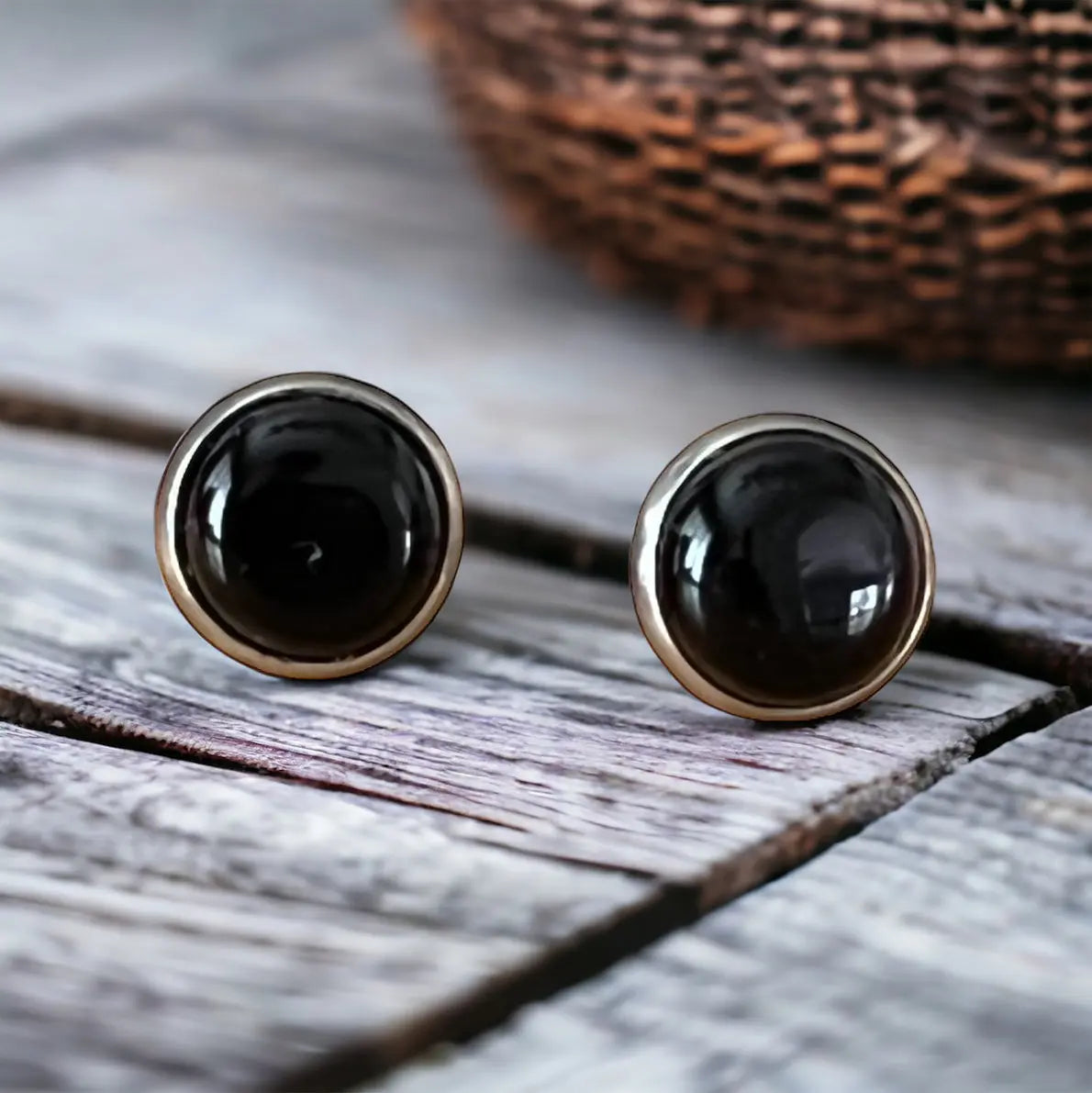 Round black onyx-style stud earrings in a silver-tone setting displayed on a light wood background