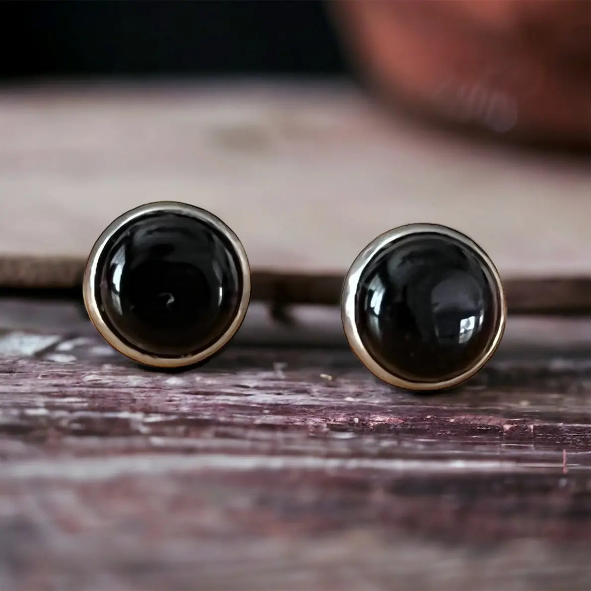Close-up of round black onyx-style stud earrings in a silver-tone setting displayed on a wood background