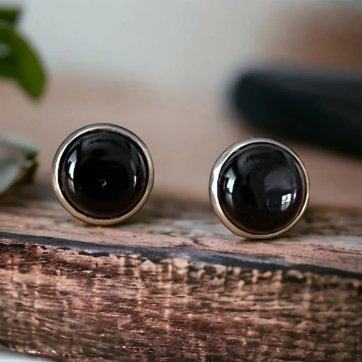 Round black onyx-style stud earrings in a silver-tone setting displayed on a wood background