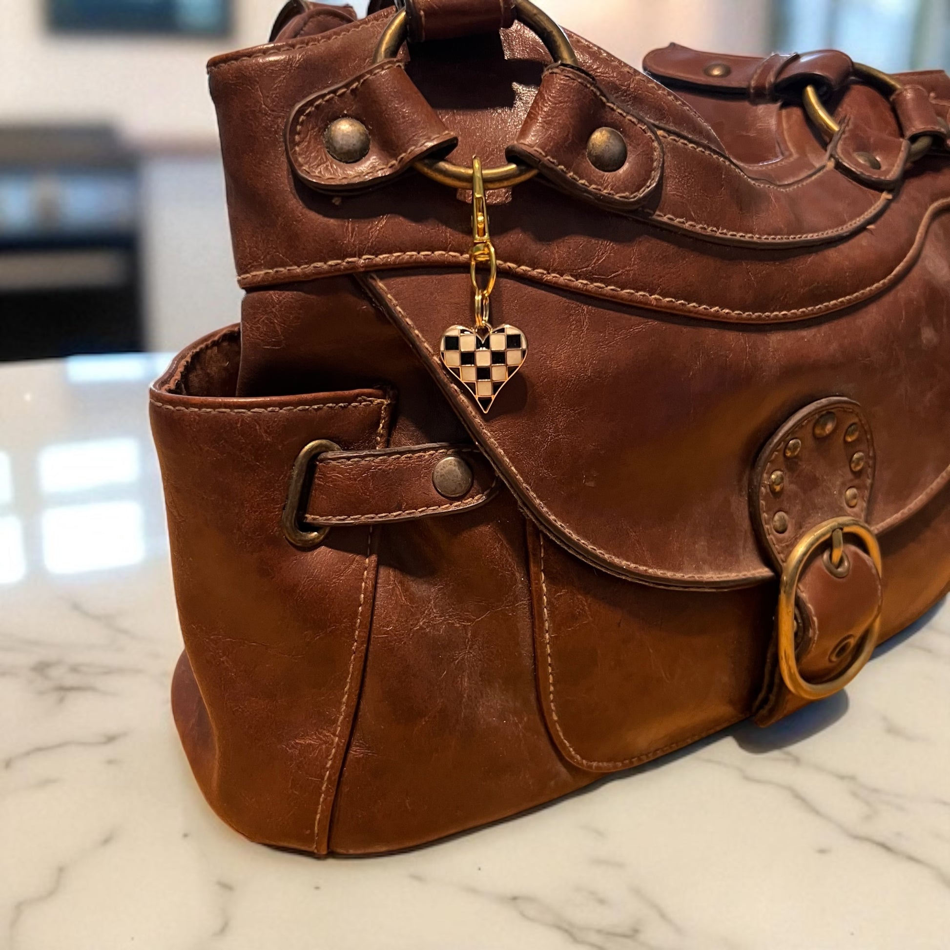 Brown leather handbag with a heart-shaped keychain on a marble surface
