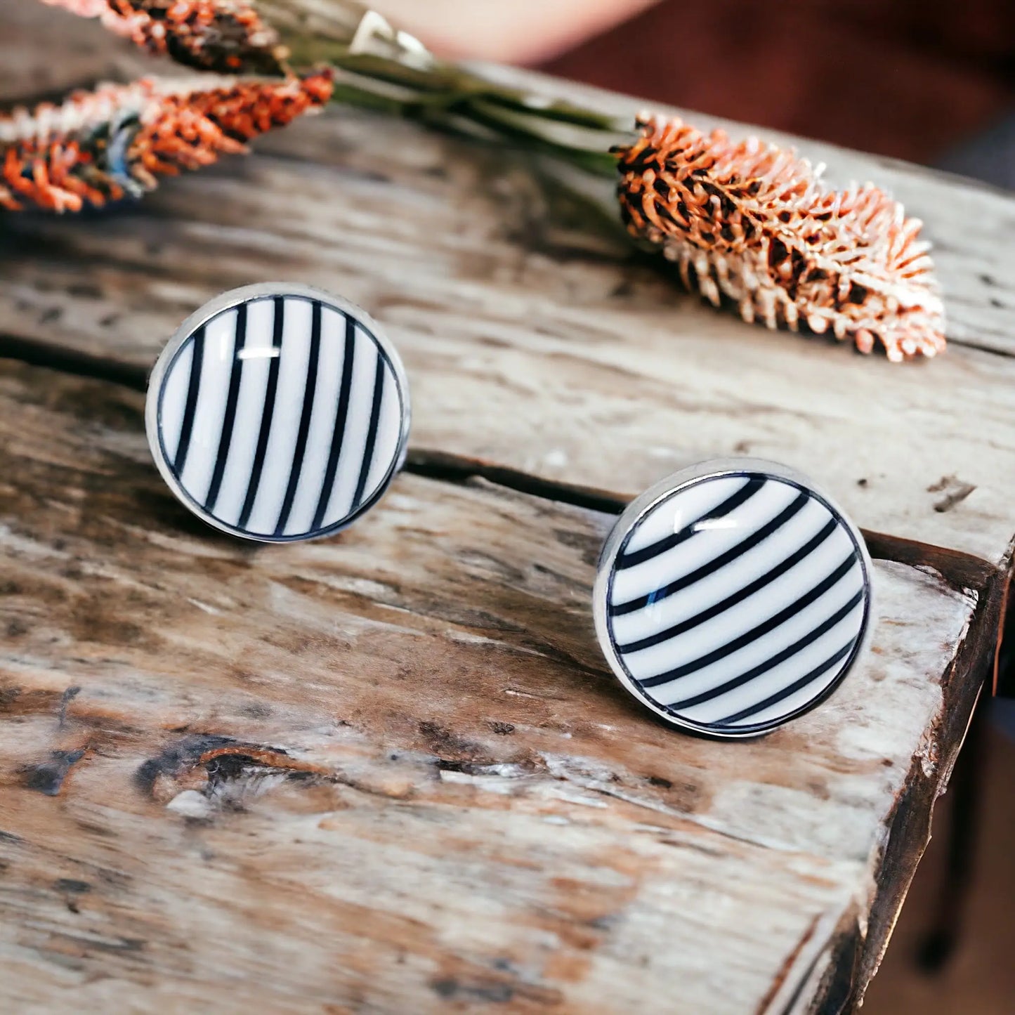 Pair of black and white striped earrings on a wooden surface with dried flowers.