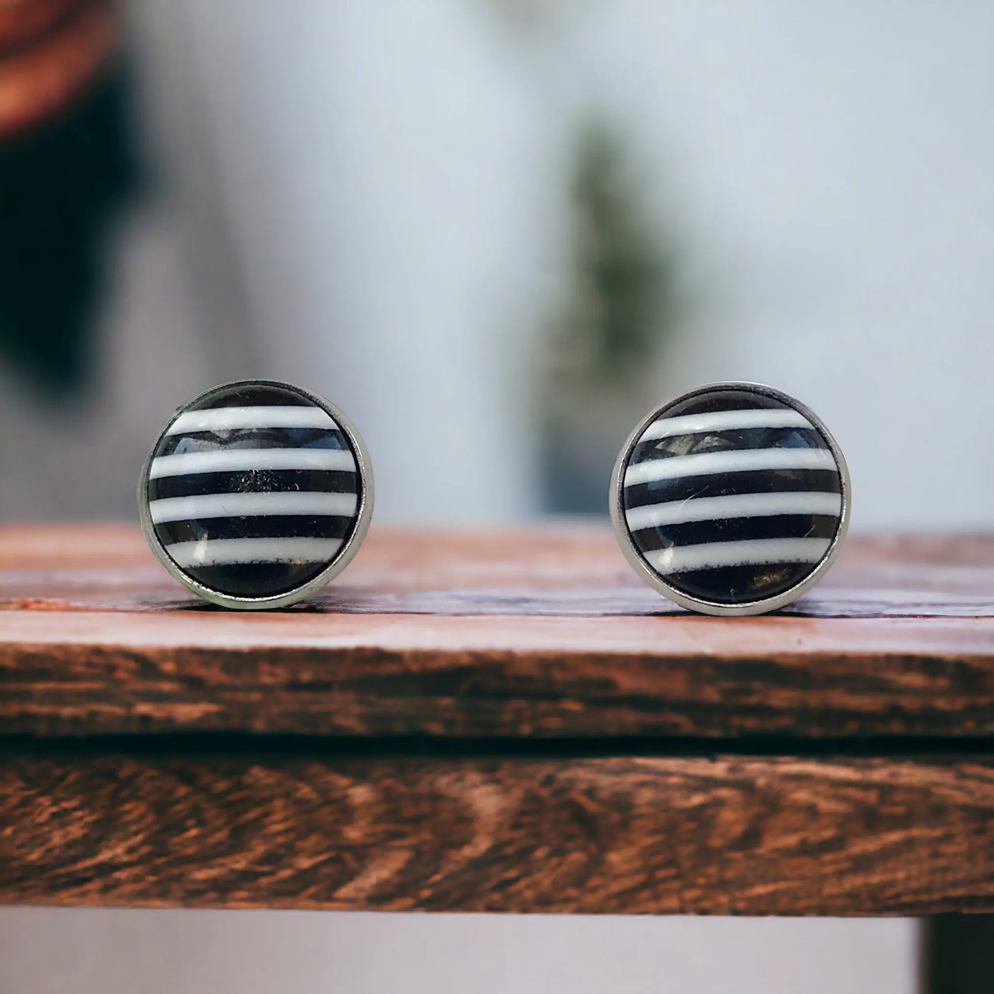 Round black and white striped stud earrings in a silver-tone setting displayed close-up on a wood surface