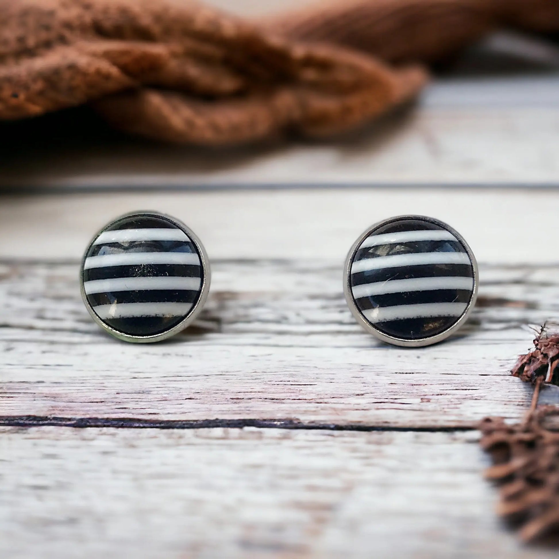 Round black and white striped stud earrings in a silver-tone setting displayed on a wood surface