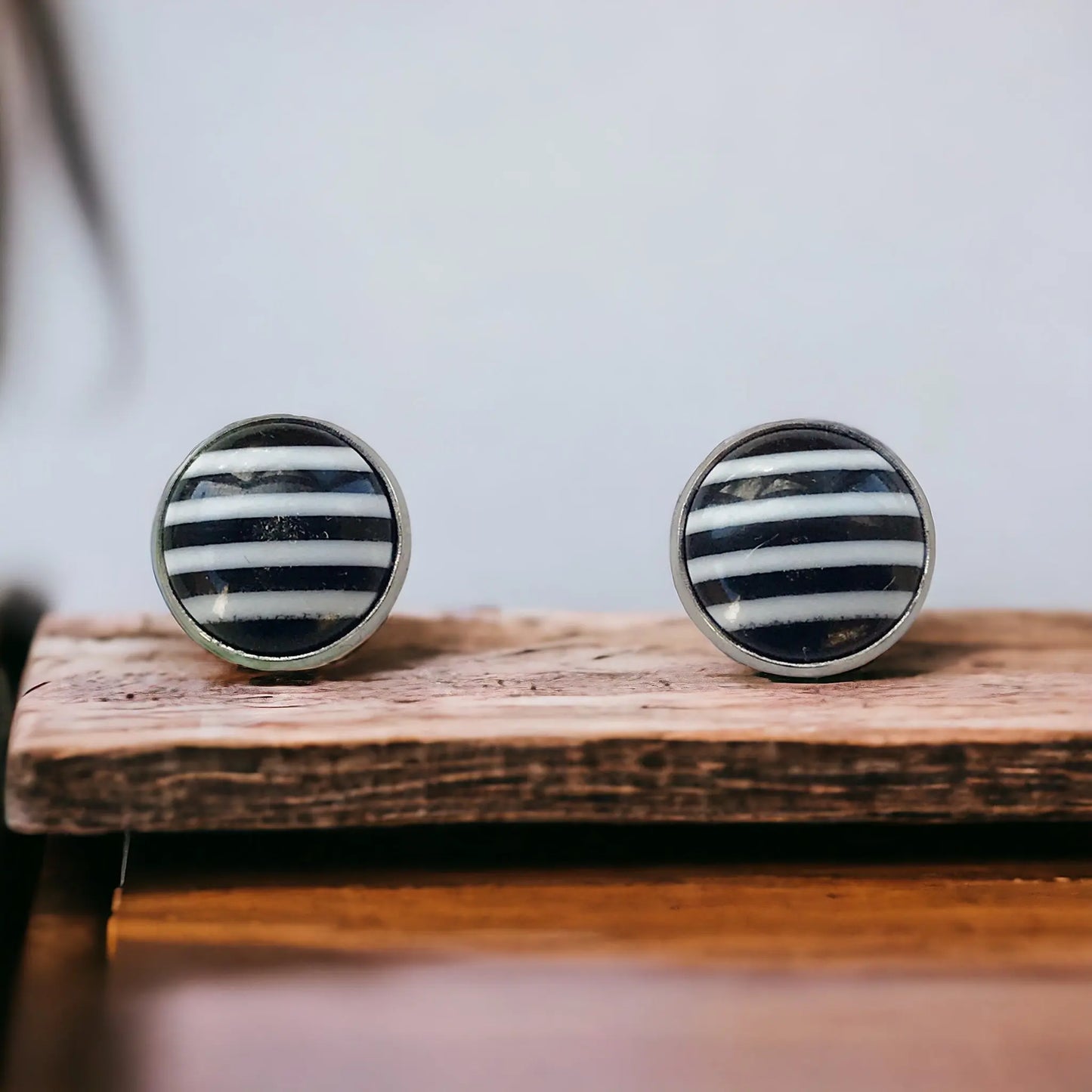 Round black and white striped stud earrings in a silver-tone setting displayed on a wood tray 