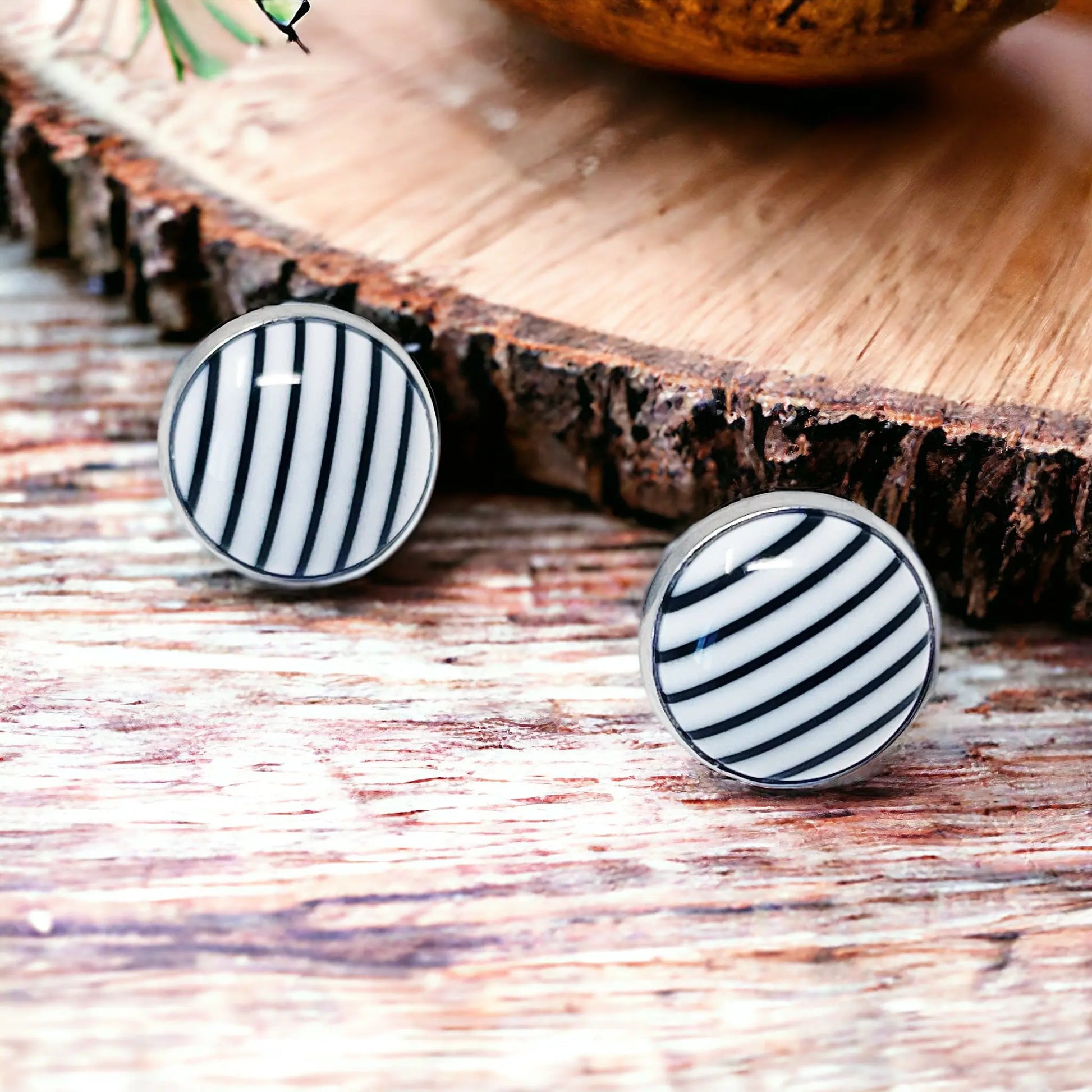 Round black and white striped stud earrings in a silver-tone setting displayed on rustic wood